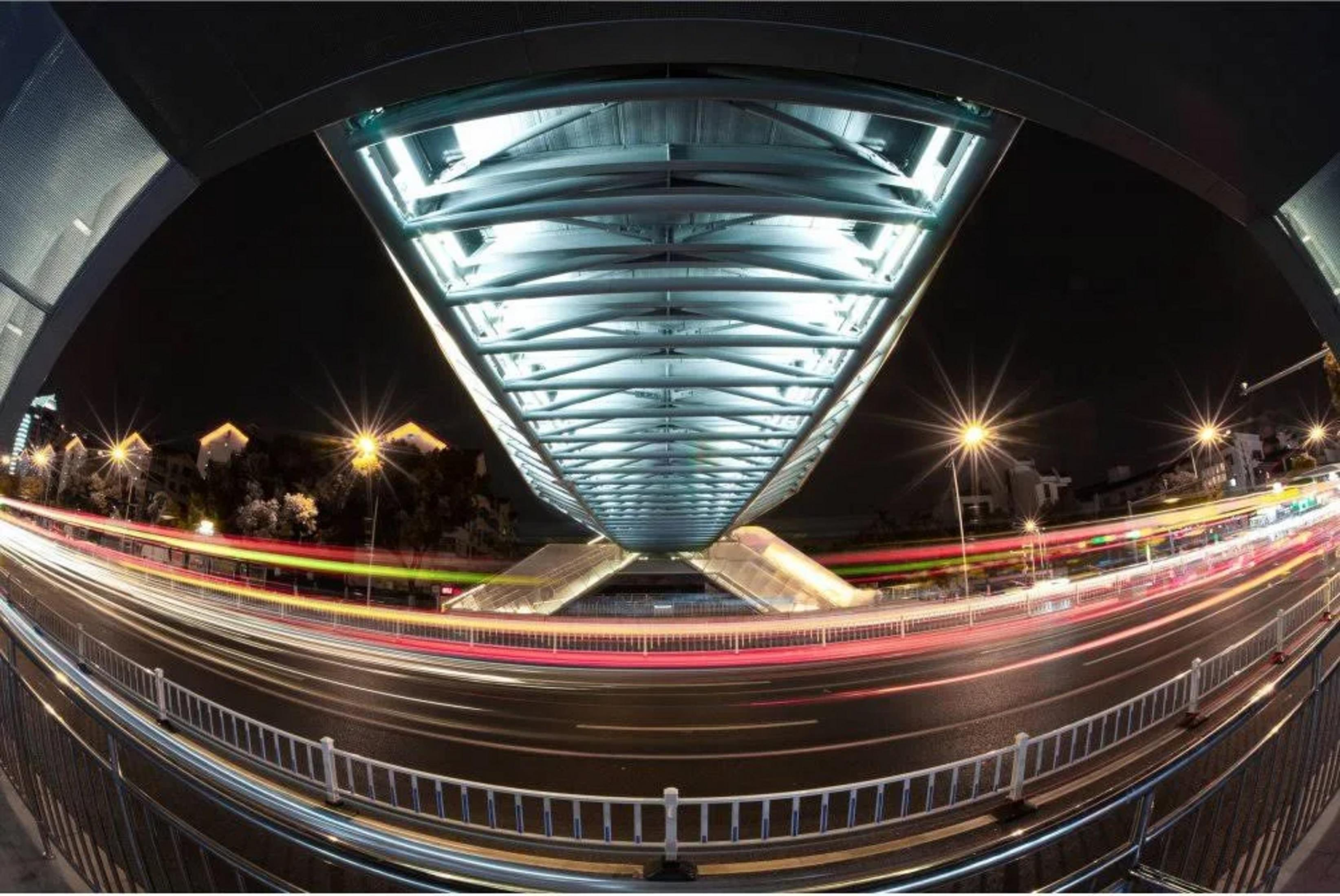 Vista fisheye di un ponte illuminato di notte, con scie luminose di auto.