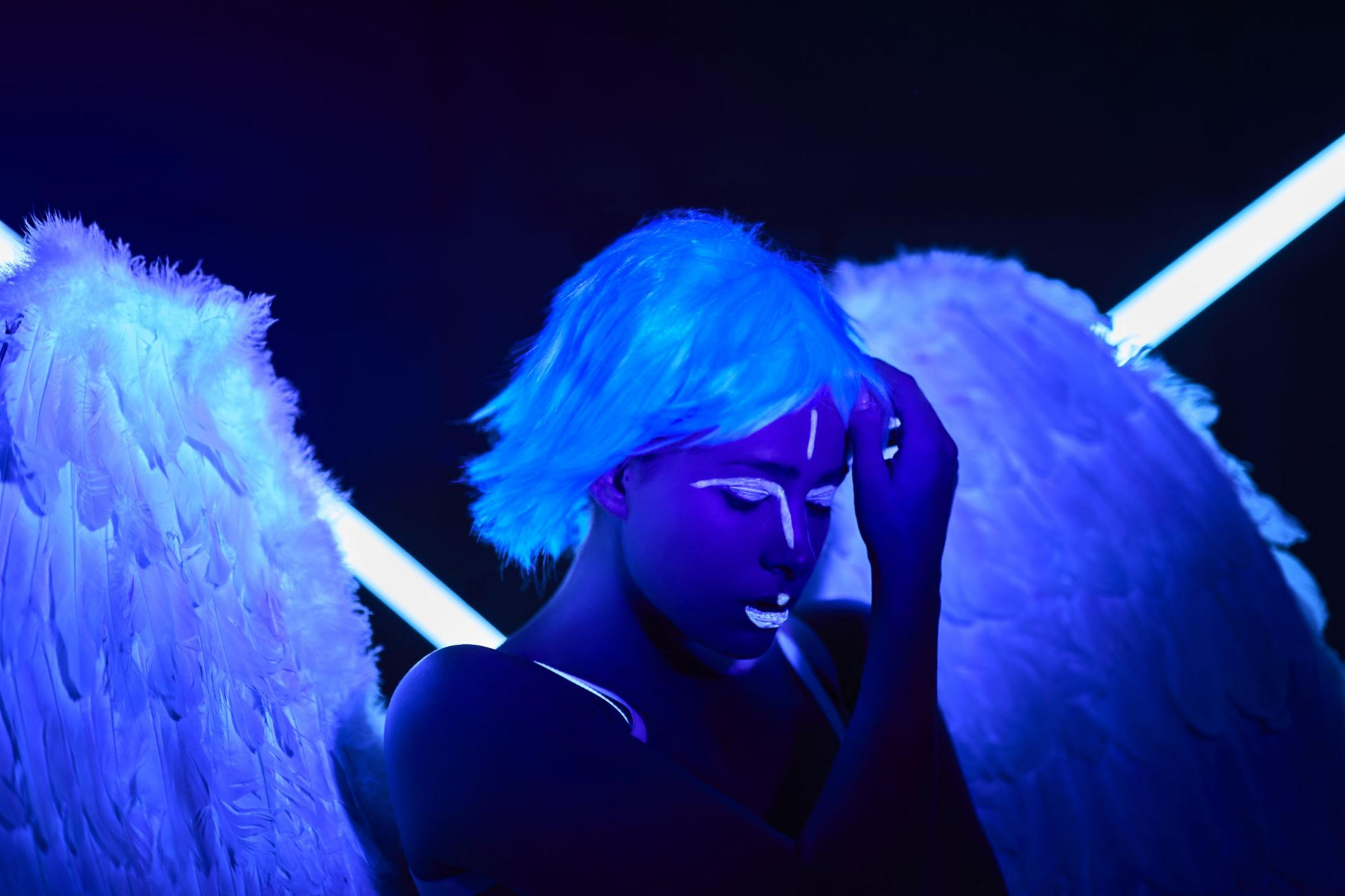 Ein Engel mit blauen Haaren und weißen Flügeln, der im blauen Licht posiert.