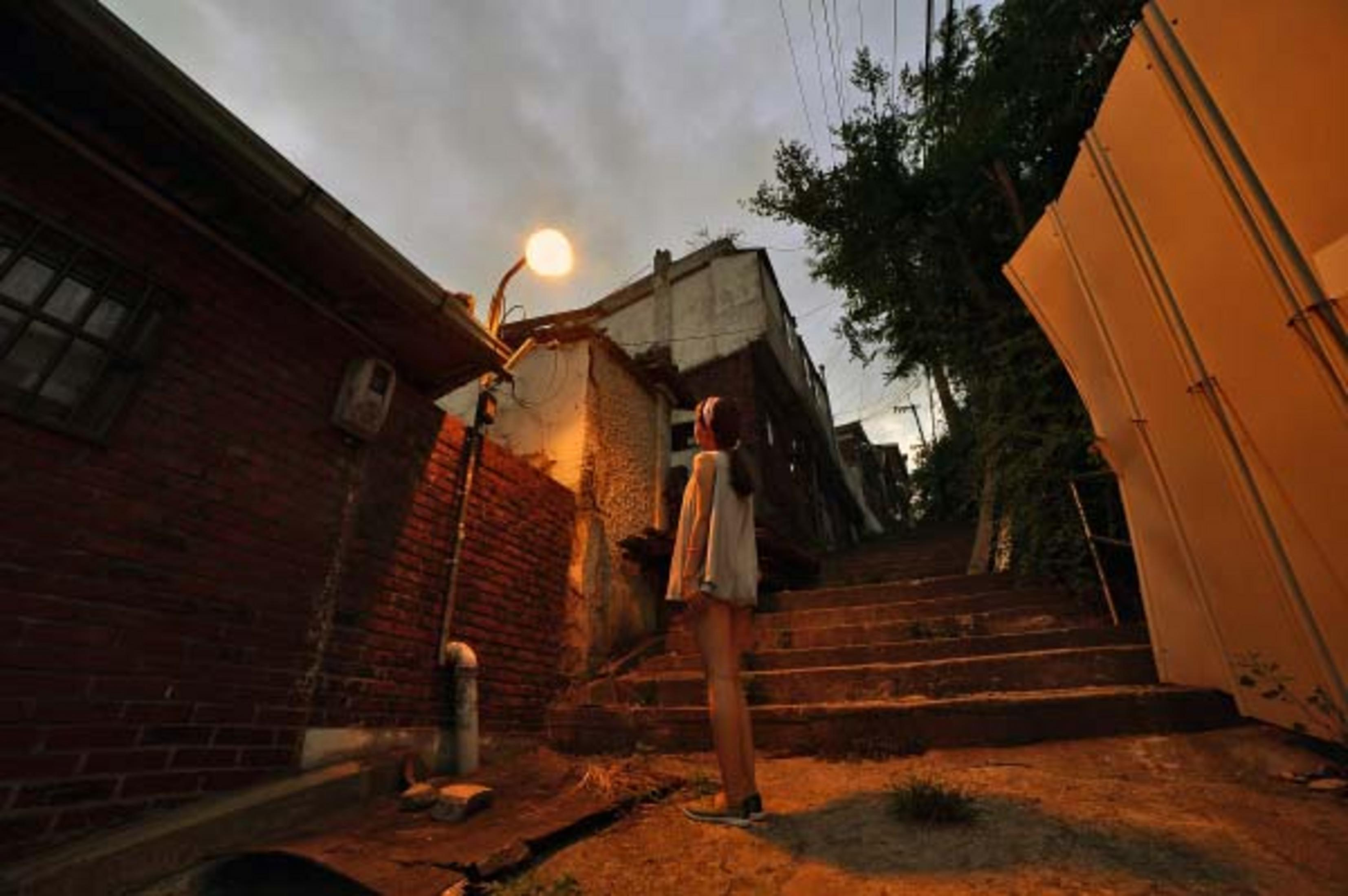 Una mujer está en escalones de piedra en un callejón de noche. Una luz está encendida.