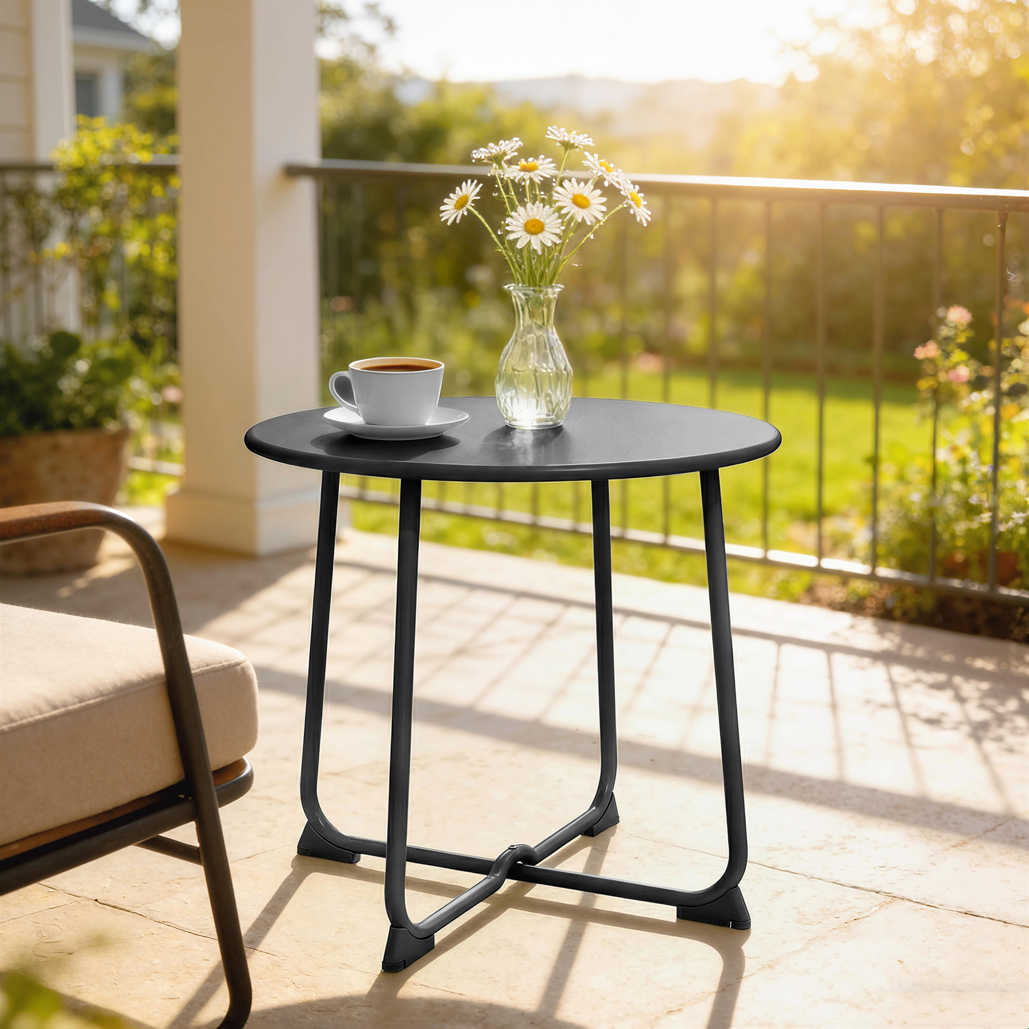 Un tavolino nero con una tazza di caffè e margherite su un patio.