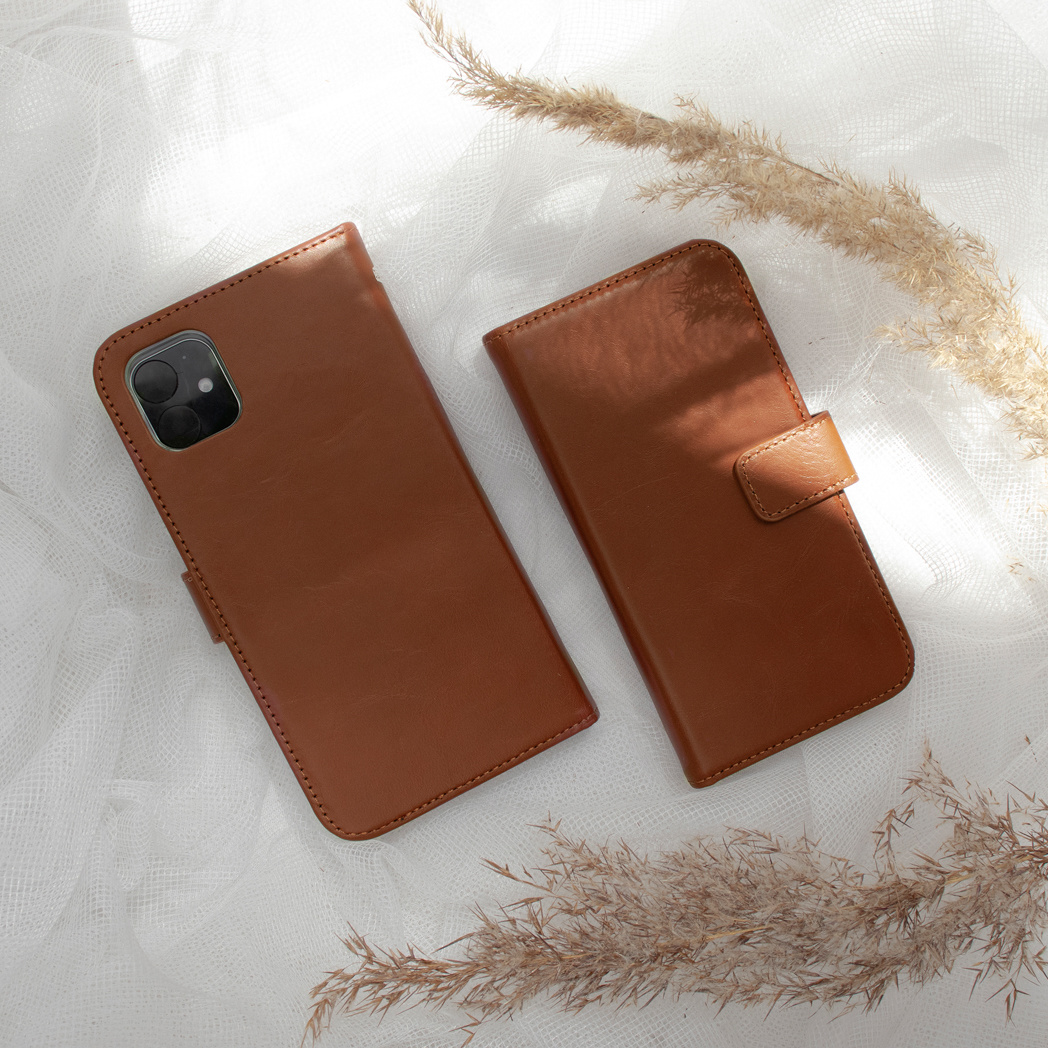 Twee bruine leren telefoonhoesjes op witte stof met gedroogde grassen.