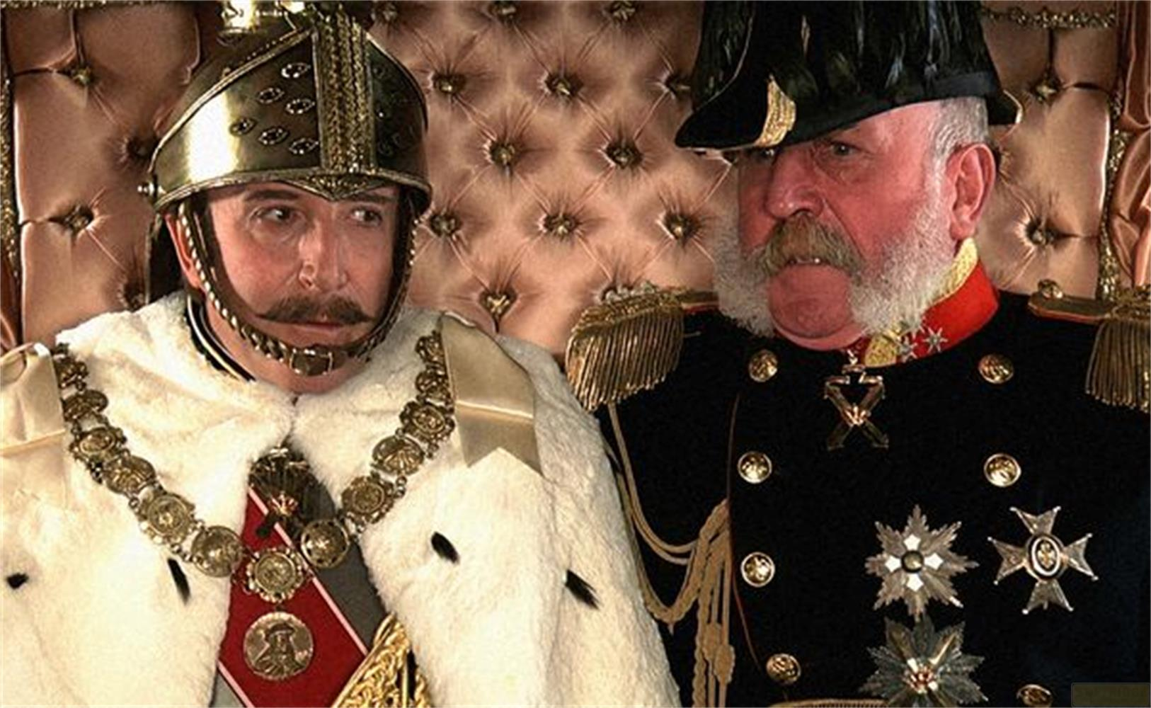 Due uomini in uniformi storiche siedono su un trono. Uno indossa un elmo dorato.