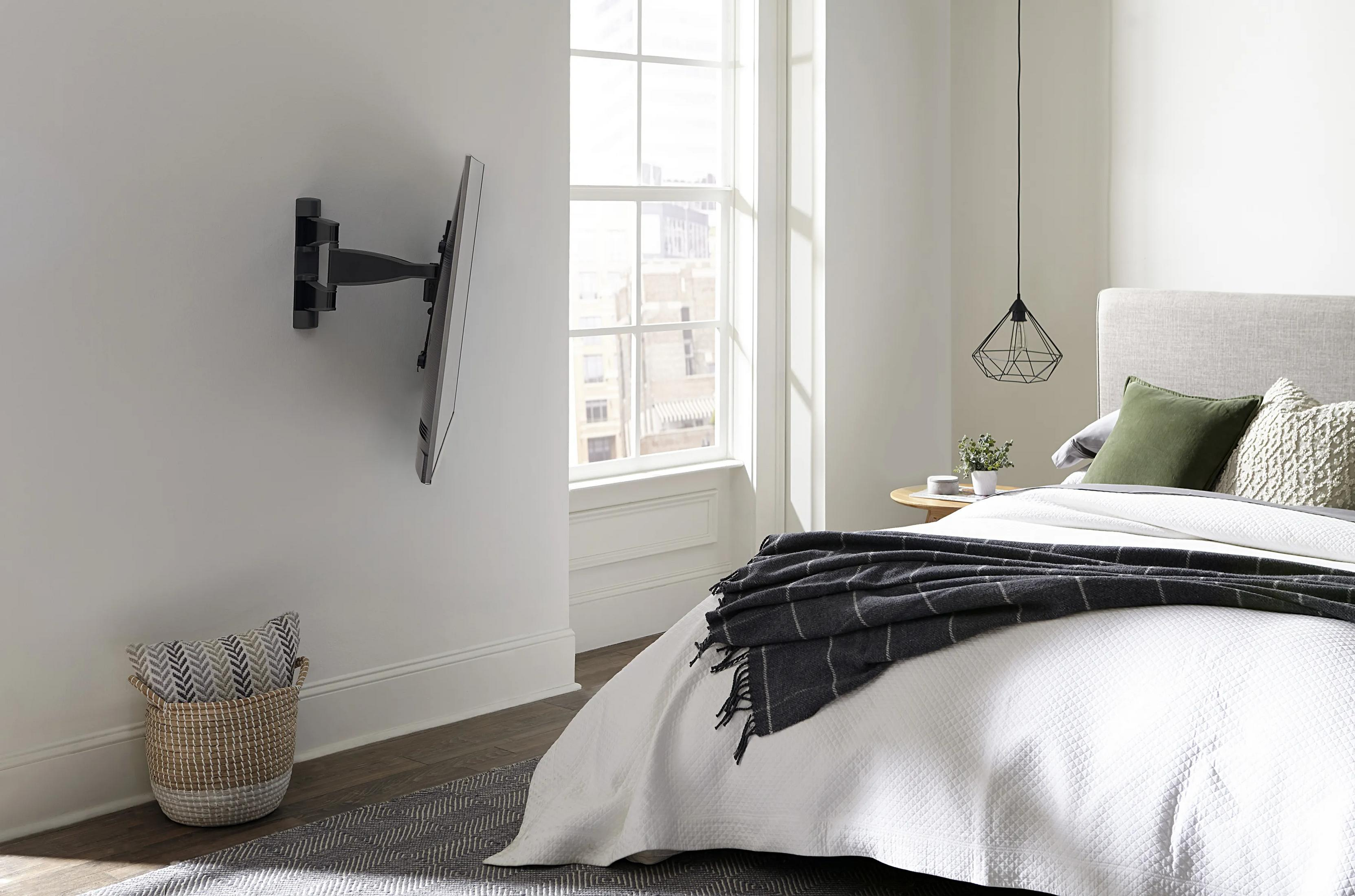 Ein Fernseher ist an der Wand montiert. Ein Bett mit Decke und Kissen ist im Raum.