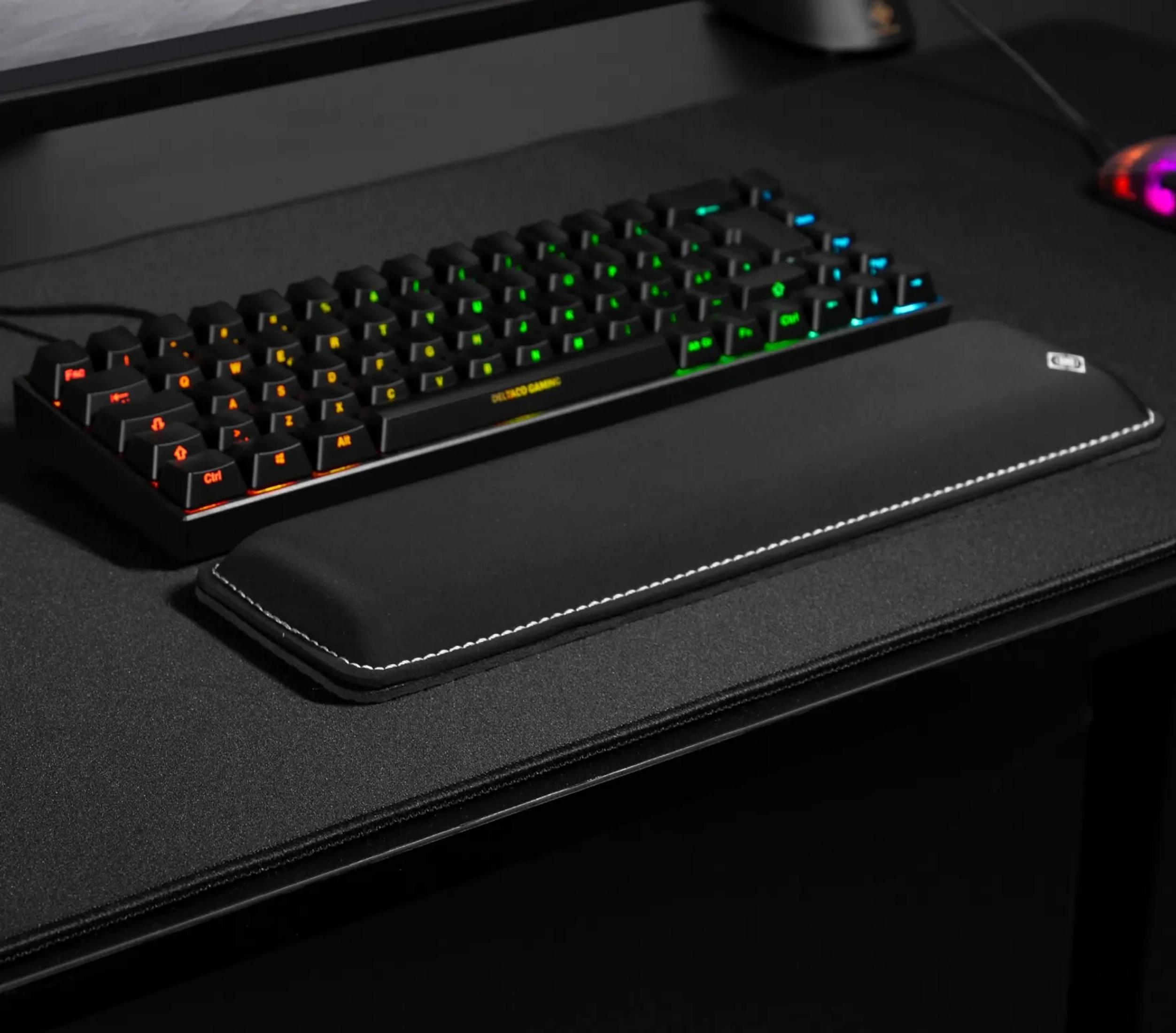 Schwarze Tastatur mit RGB-Beleuchtung und Handgelenkauflage auf einer Matte.