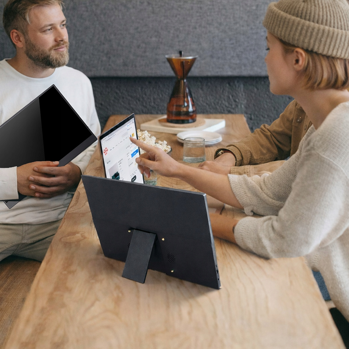 Dwie osoby siedzą przy drewnianym stole, pracując na laptopach. Mężczyzna trzyma laptopa.