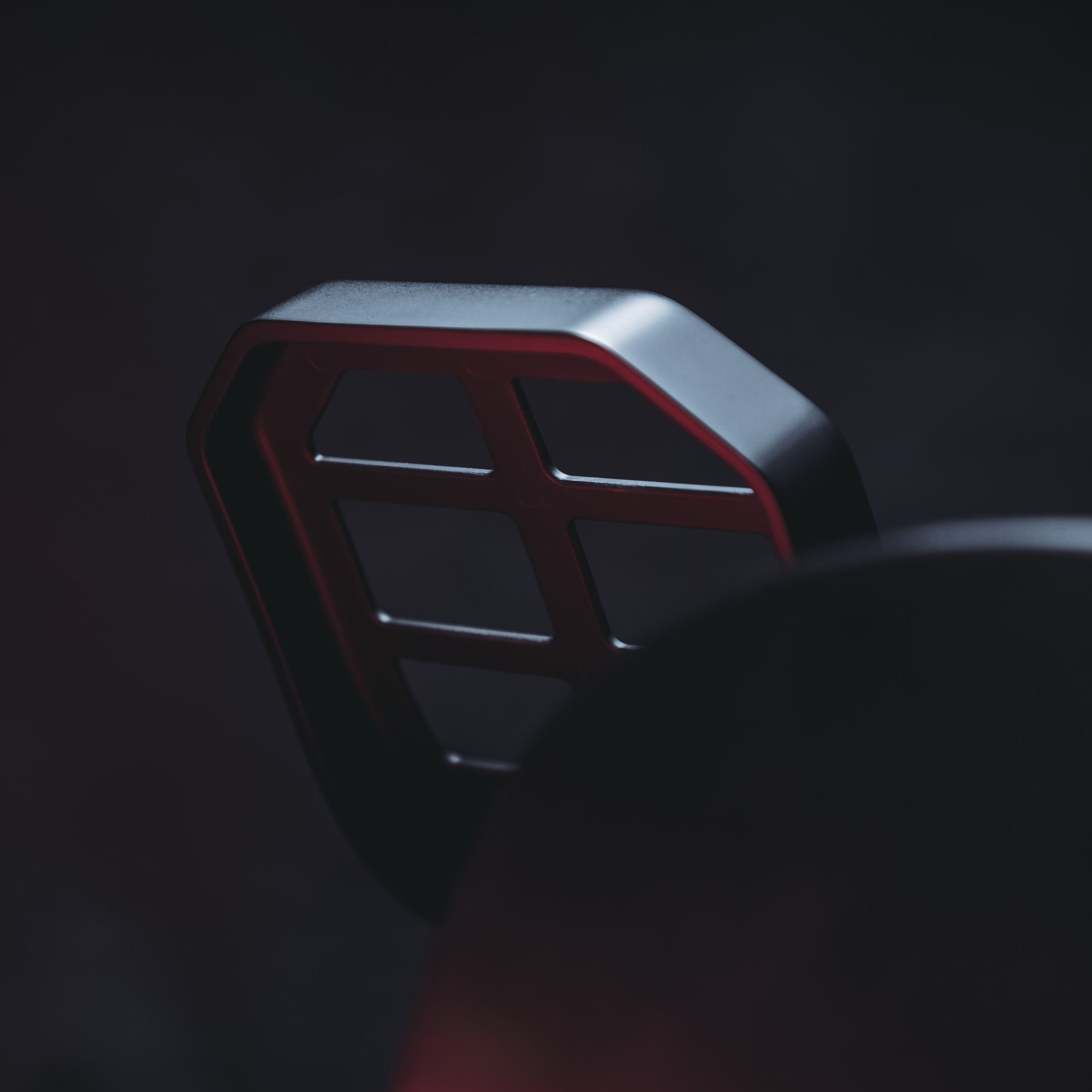 Close-up of a dark metallic object with red accents and a grid pattern.