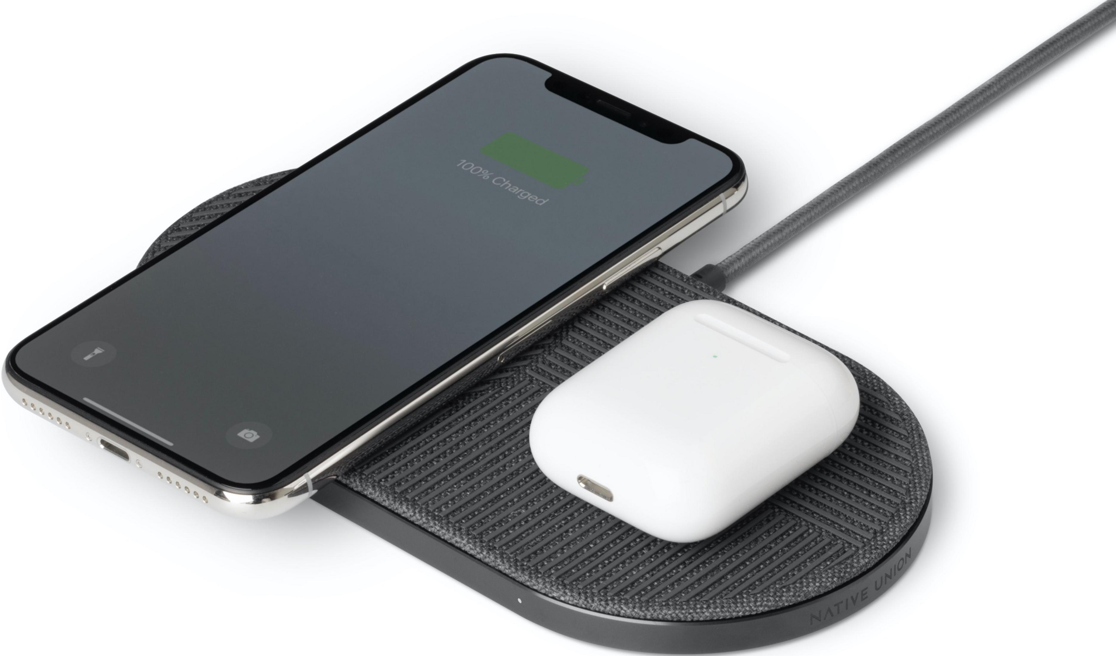 Un iPhone indiquant 100% chargé et des AirPods sur un chargeur gris.