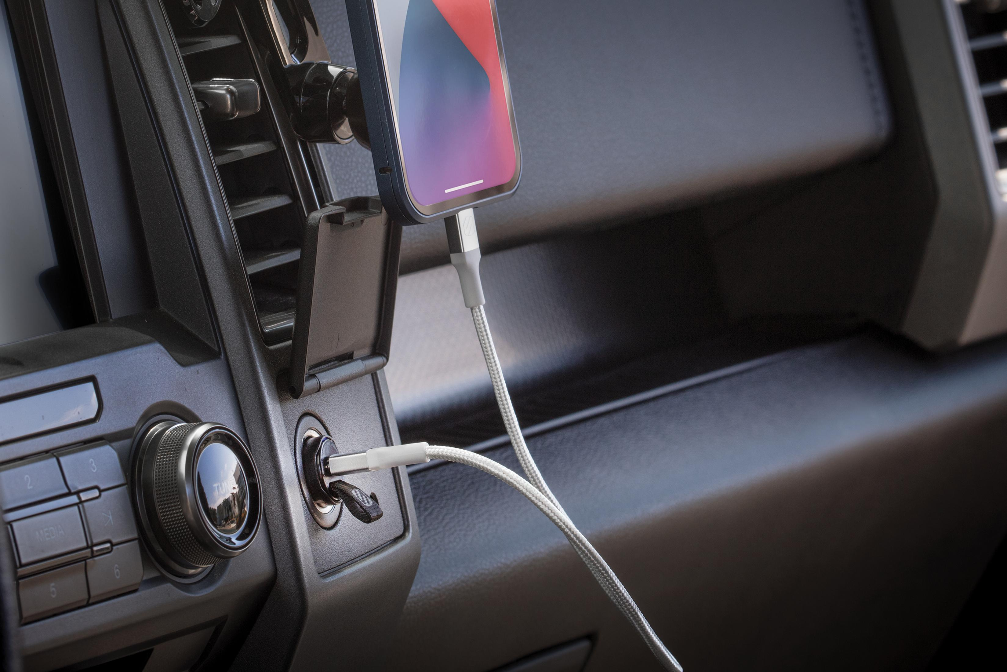 Ein Handy wird im Auto über ein weißes Kabel aufgeladen, das in den Aux-Anschluss gesteckt ist.
