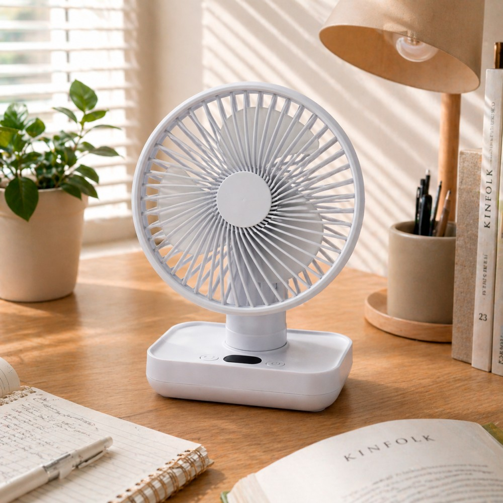 Un pequeño ventilador blanco está sobre un escritorio de madera junto a una planta y libros.