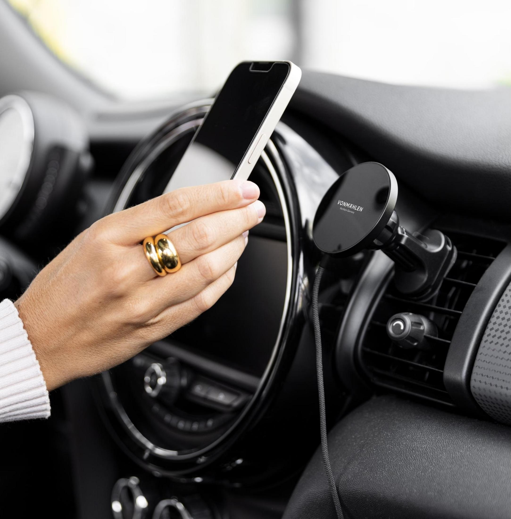Hand hält Smartphone vor Auto-Armaturenbrett mit Handyhalterung.