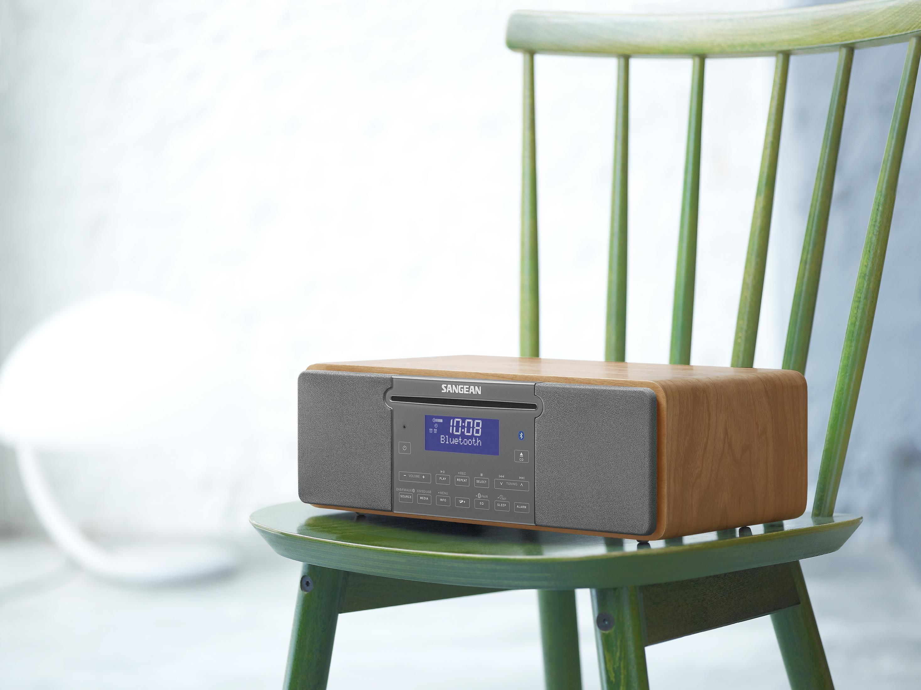 Une radio en bois avec des haut-parleurs gris est assise sur une chaise verte.