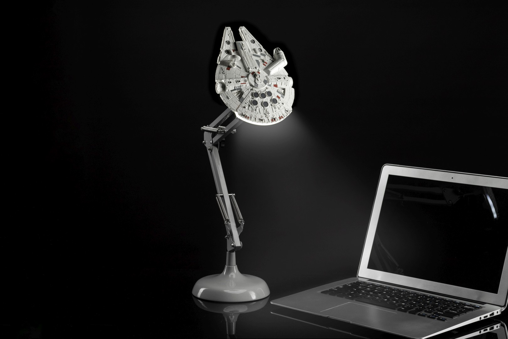 Biała lampa Millennium Falcon świeci na laptopie na czarnym tle.