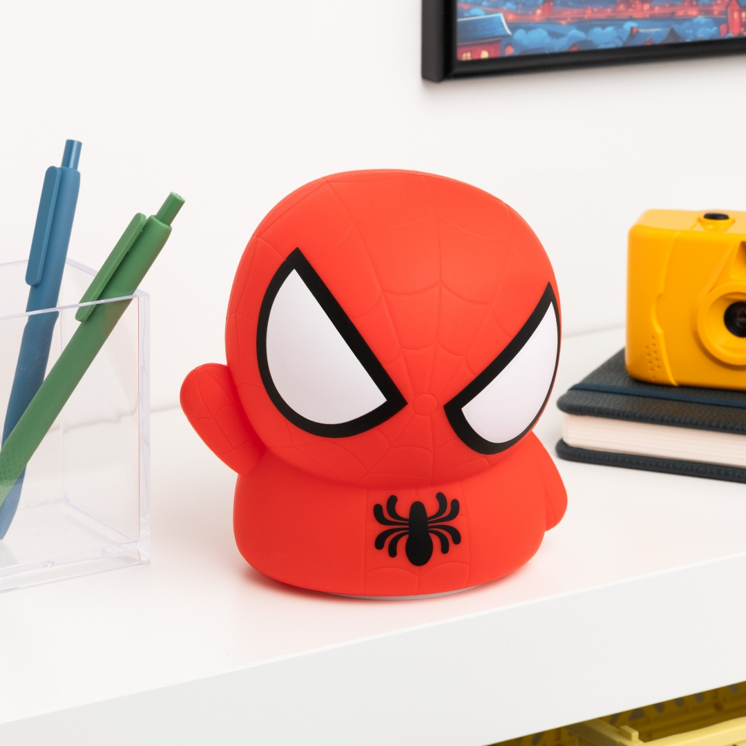 Czerwona figurka Spidermana z dużymi oczami siedzi obok długopisów i książek.