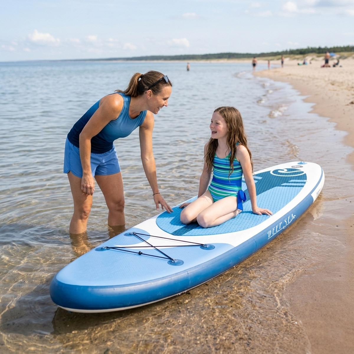 Kobieta i dziewczynka na desce SUP na plaży. Kobieta w niebieskich szortach i topie, dziewczynka w stroju kąpielowym.