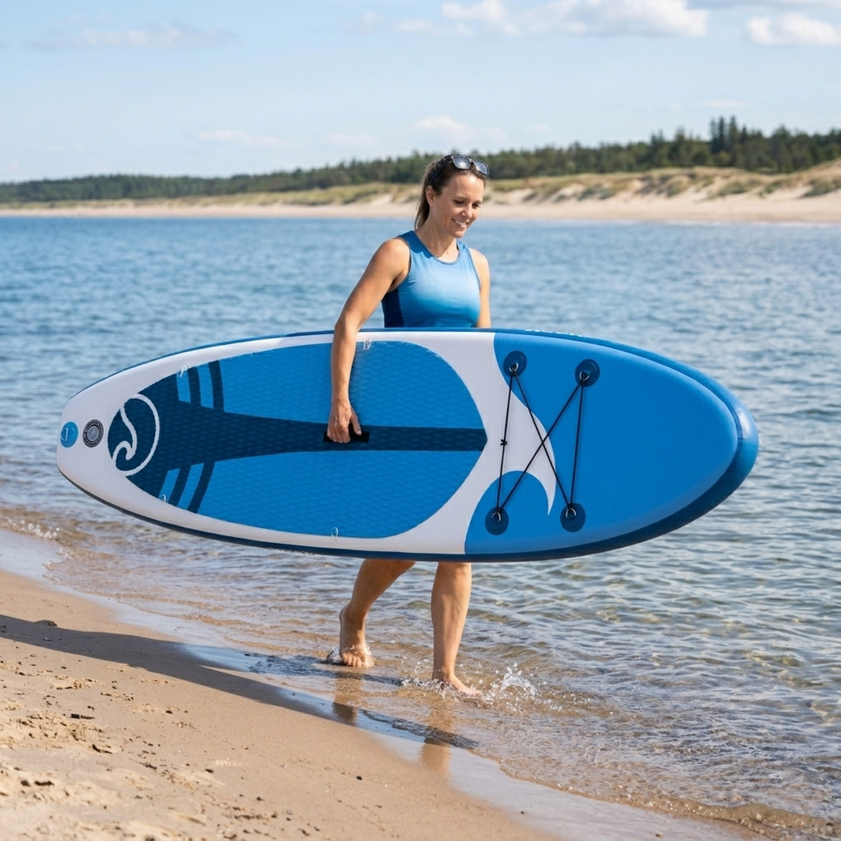 Kobieta niesie niebiesko-białą deskę SUP do wody na plaży.