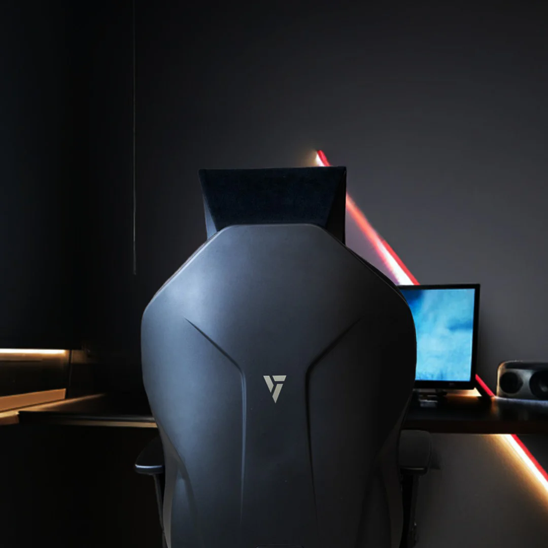 Una silla gamer negra con logo plateado frente a un monitor de computadora.
