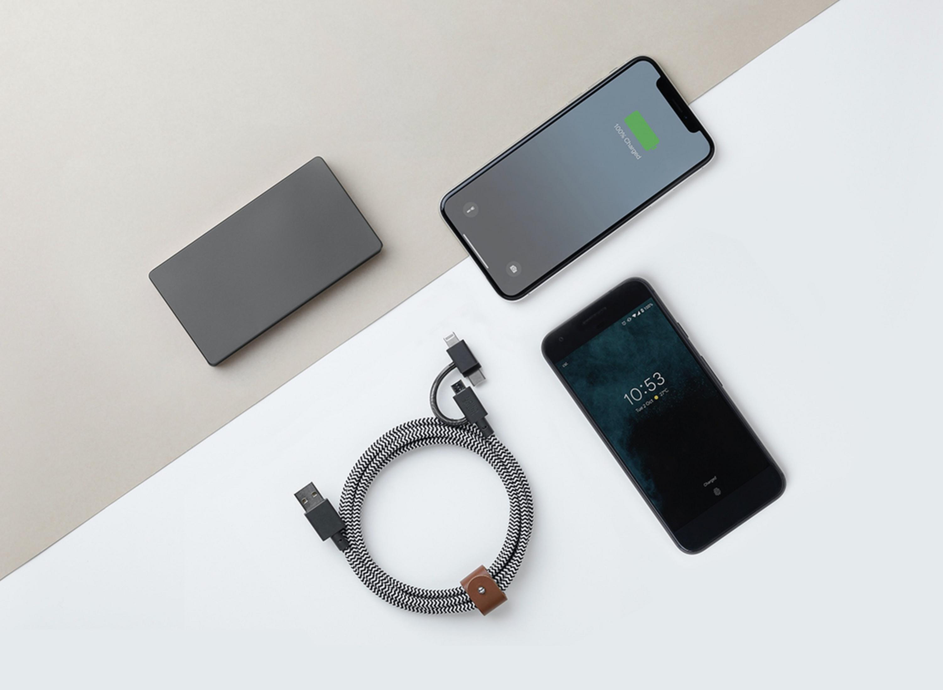 Un power bank grigio, un cavo di ricarica e due smartphone giacciono su uno sfondo bicolore.