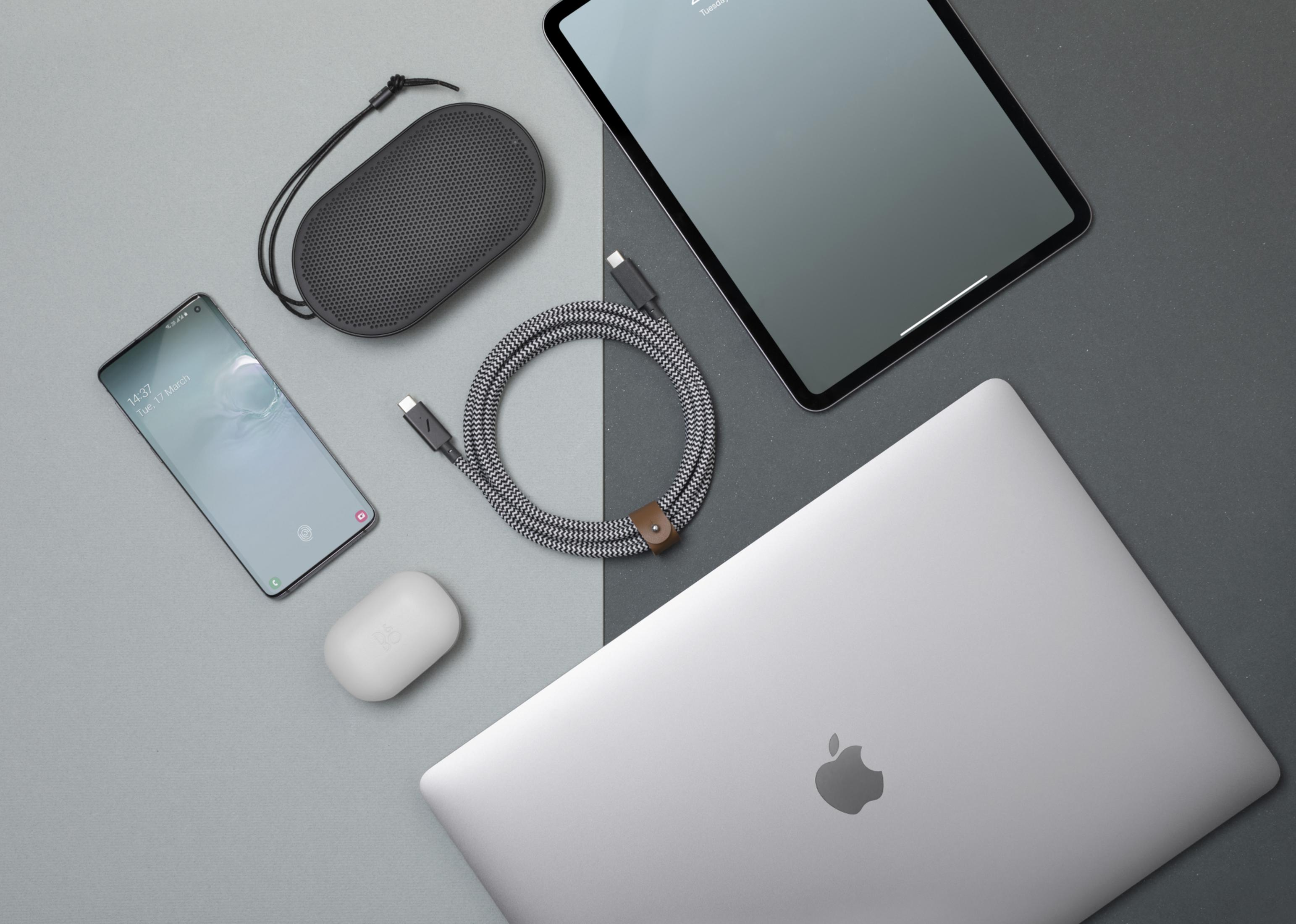 Un laptop, tablet, smartphone, altoparlante, auricolari e cavo disposti su superfici grigie.