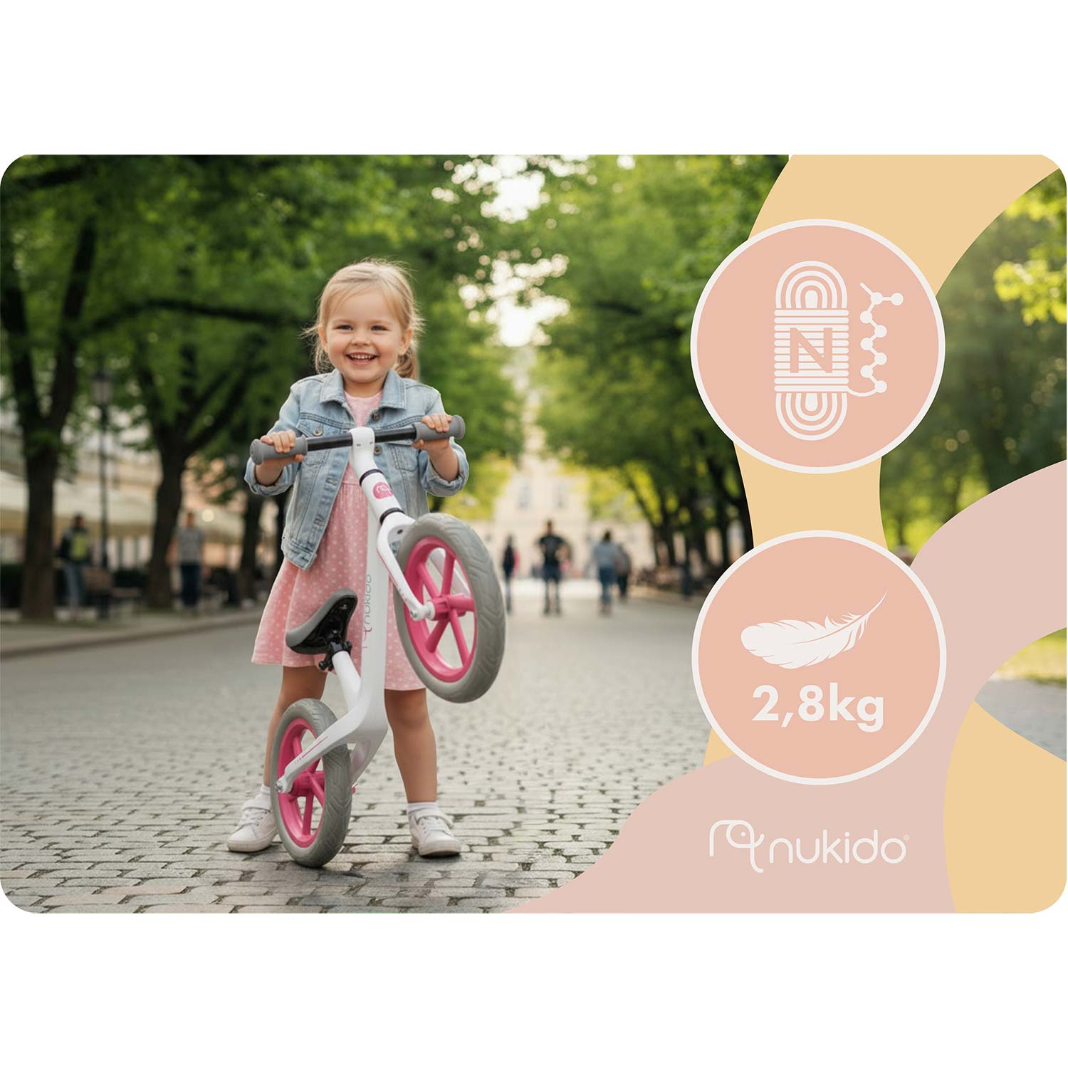 Uśmiechnięta dziewczynka z rowerkiem biegowym na zewnętrznej, brukowanej ulicy.