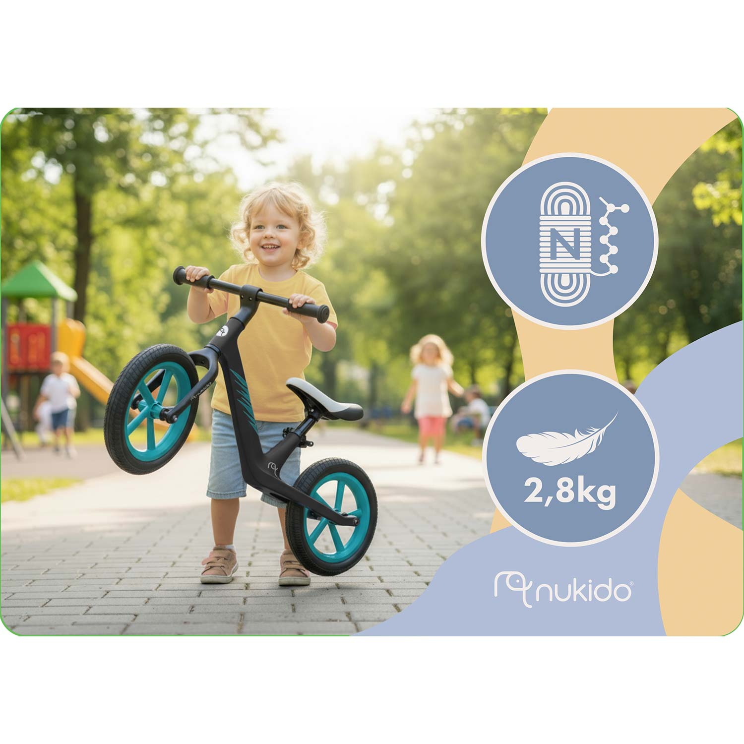 Małe dziecko z rowerkiem biegowym na ścieżce, plac zabaw w tle.