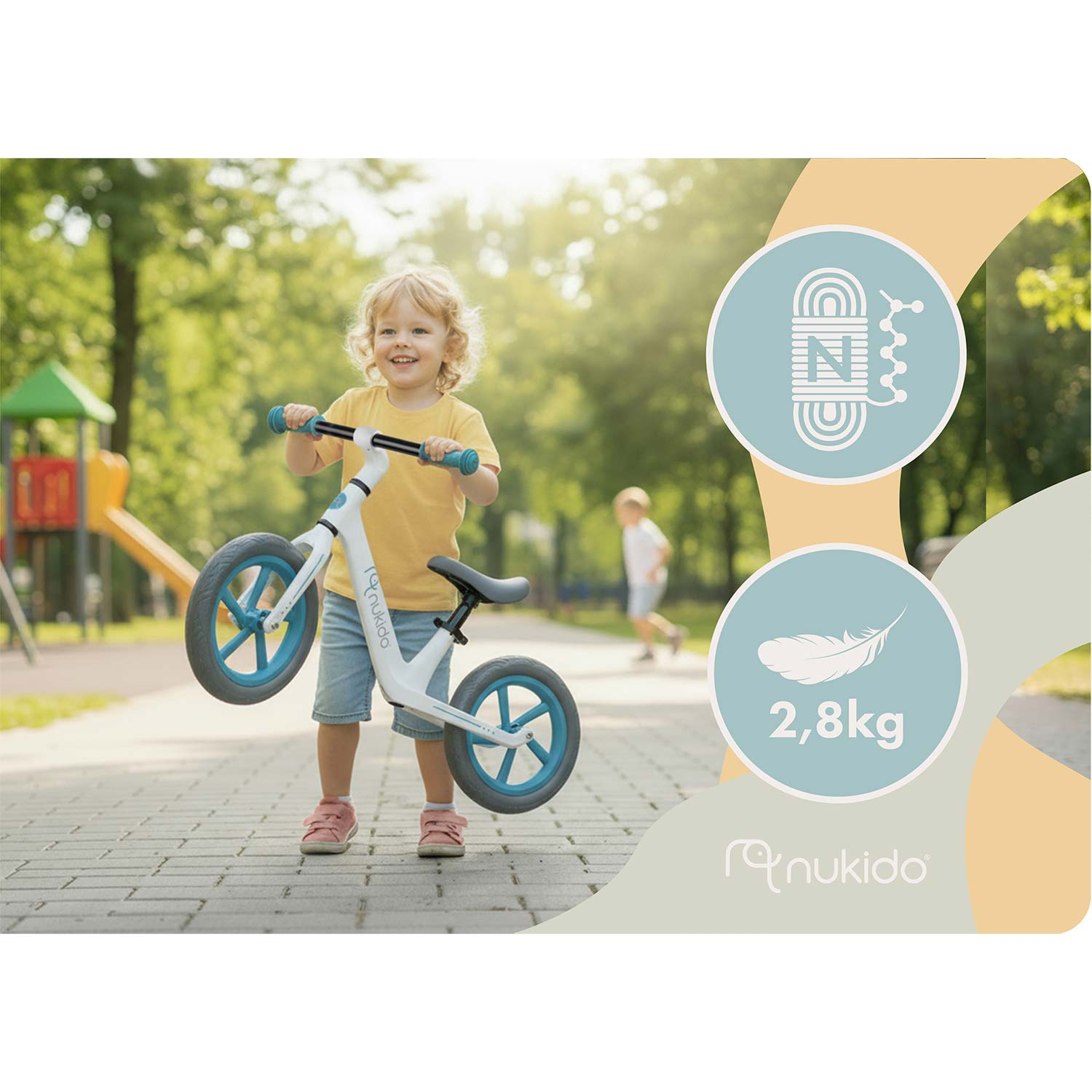 Uśmiechnięte dziecko w żółtej koszulce trzyma biały rowerek biegowy z niebieskimi kołami na brukowanej ścieżce.