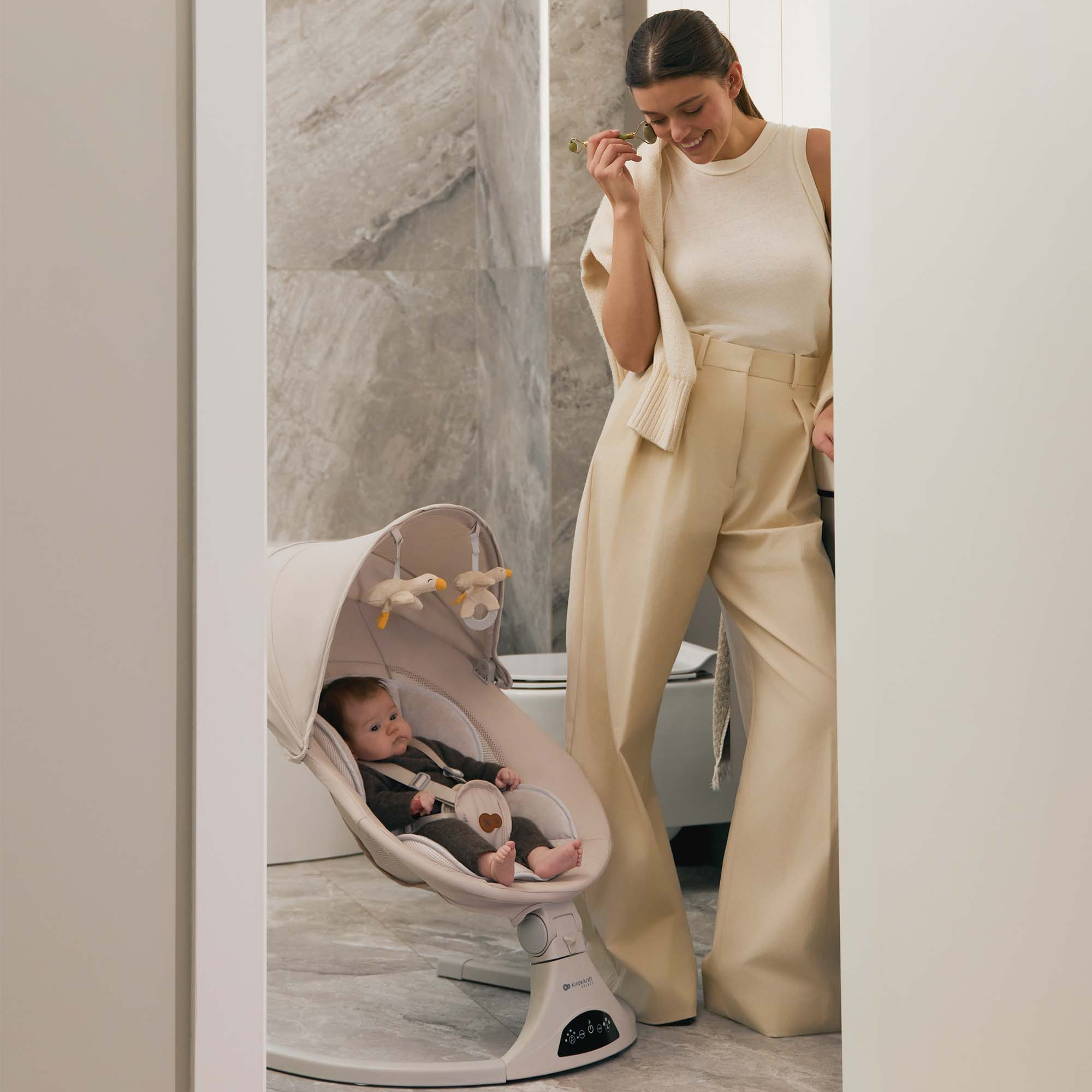 Eine Frau pflegt ihr Gesicht, während ein Baby in einer Babywippe liegt.