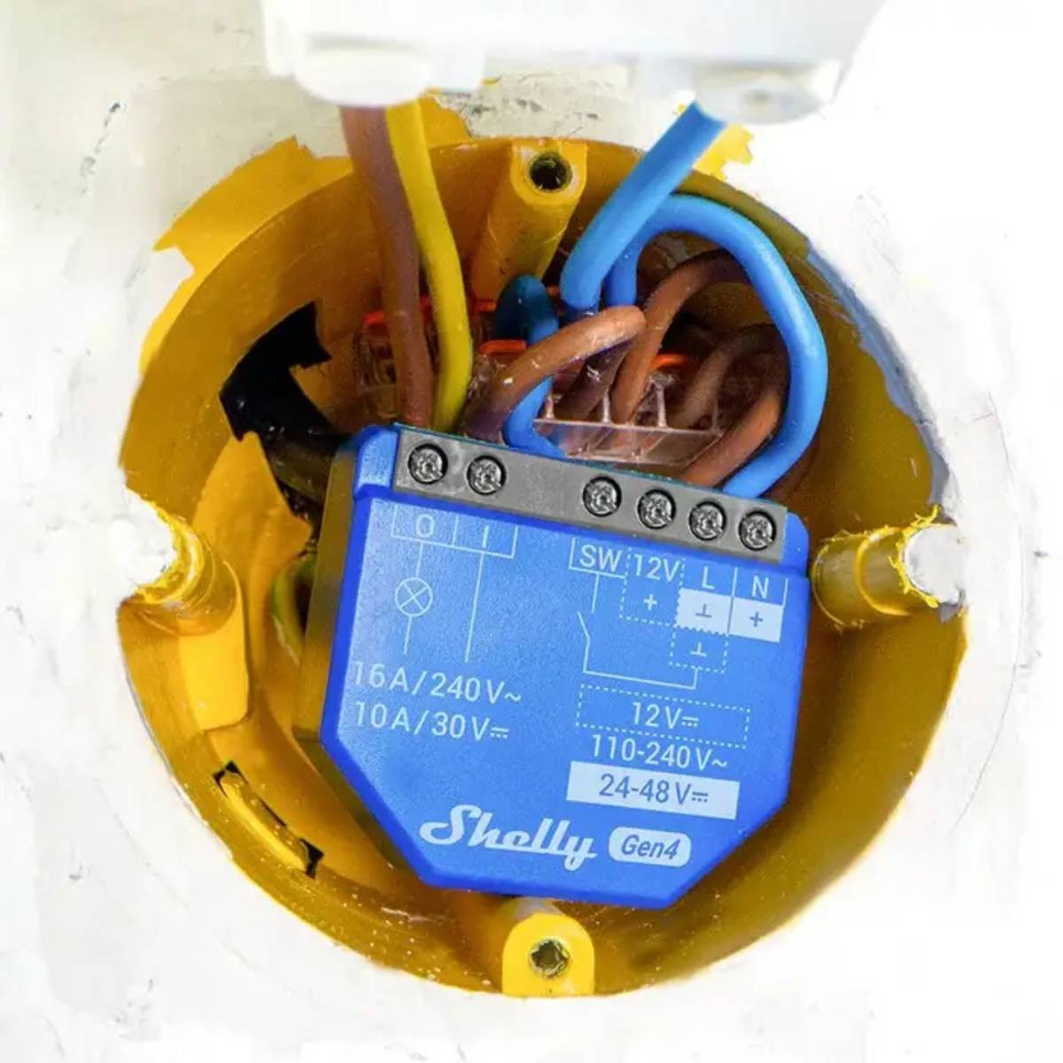 Moduł Shelly Gen4 z niebieską obudową, podłączony w żółtej puszce elektrycznej.