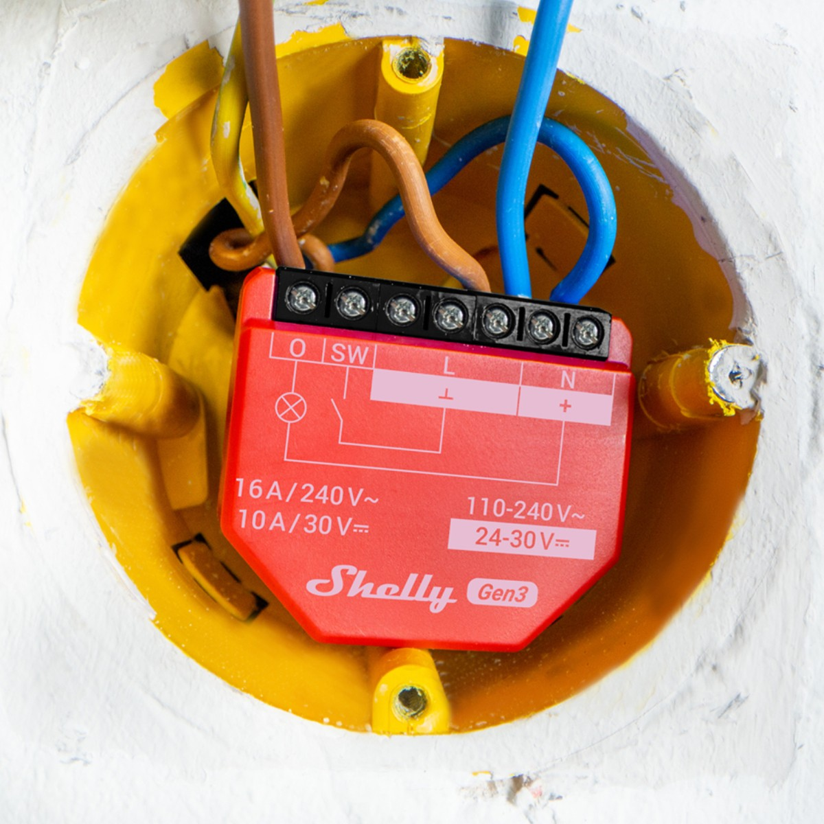 Czerwone urządzenie Shelly Gen3 z podłączonymi przewodami w żółtej skrzynce elektrycznej.