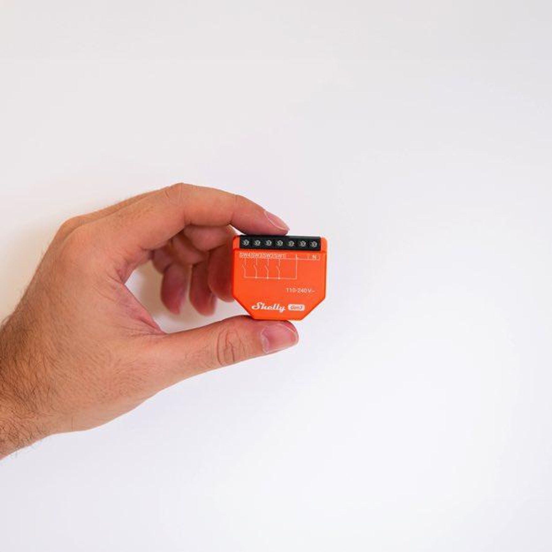 Dłoń trzyma mały, pomarańczowy przełącznik smart home Shelly Gen3.