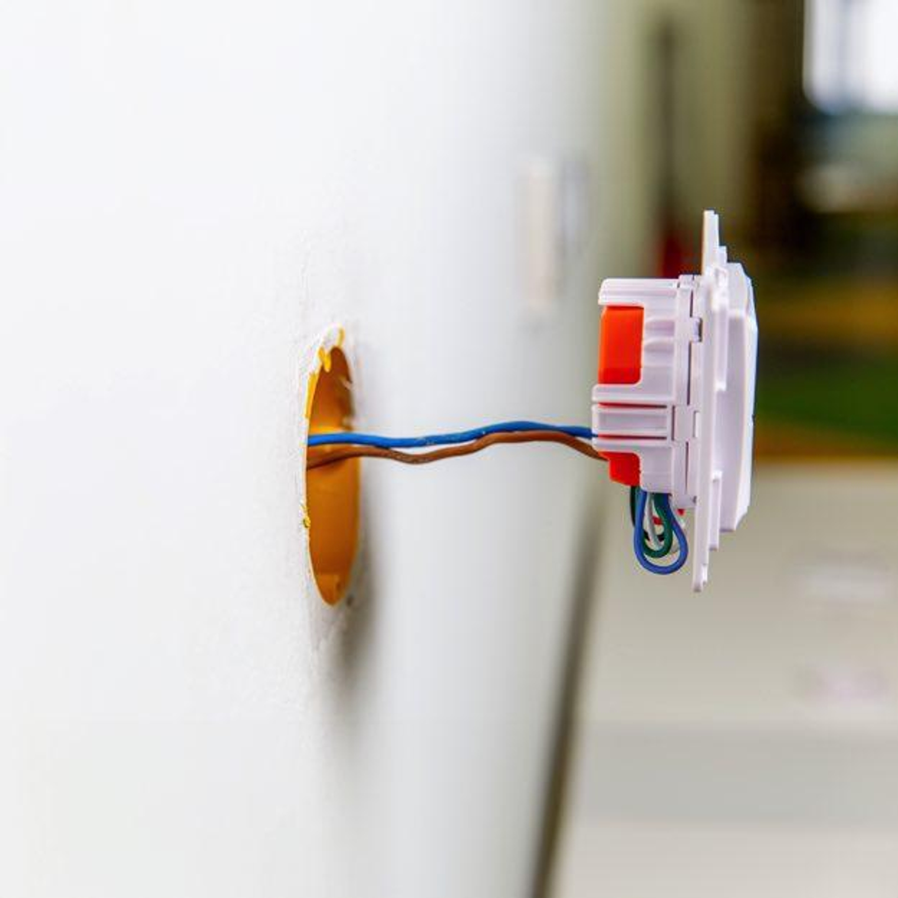 Instalacja gniazdka elektrycznego z odsłoniętymi przewodami w białej ścianie.