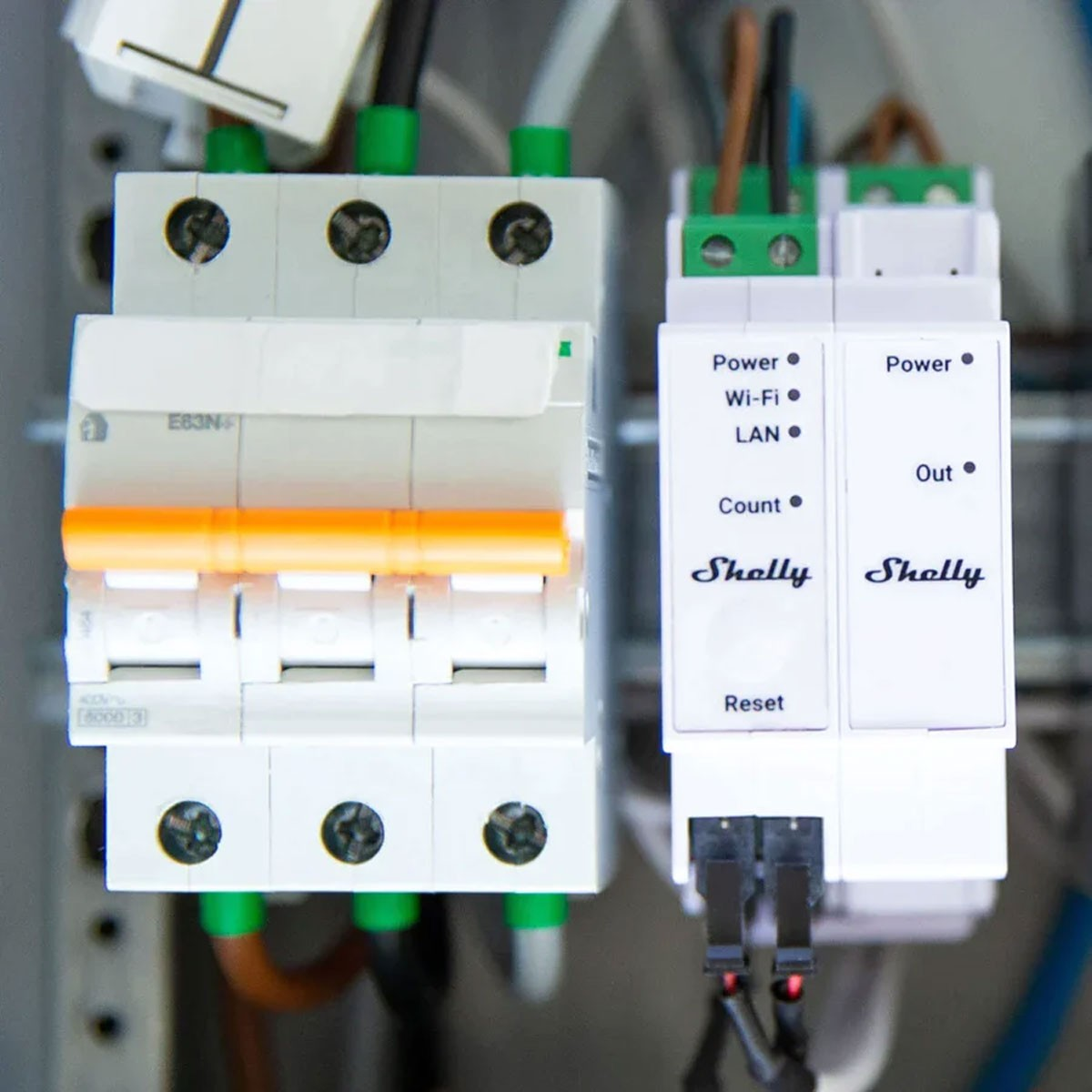 Biały wyłącznik elektryczny z pomarańczowym przełącznikiem obok dwóch białych inteligentnych przekaźników.