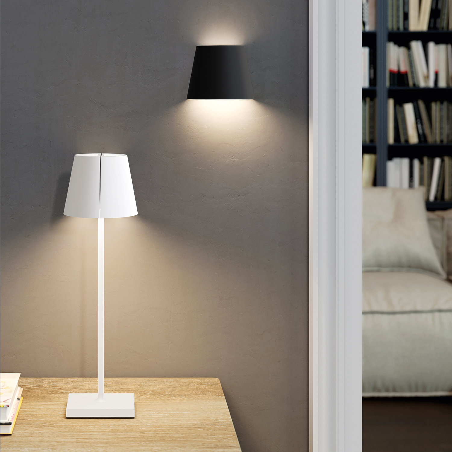 Eine weiße Tischlampe leuchtet auf einem Holztisch. Eine schwarze Wandlampe beleuchtet die Wand.