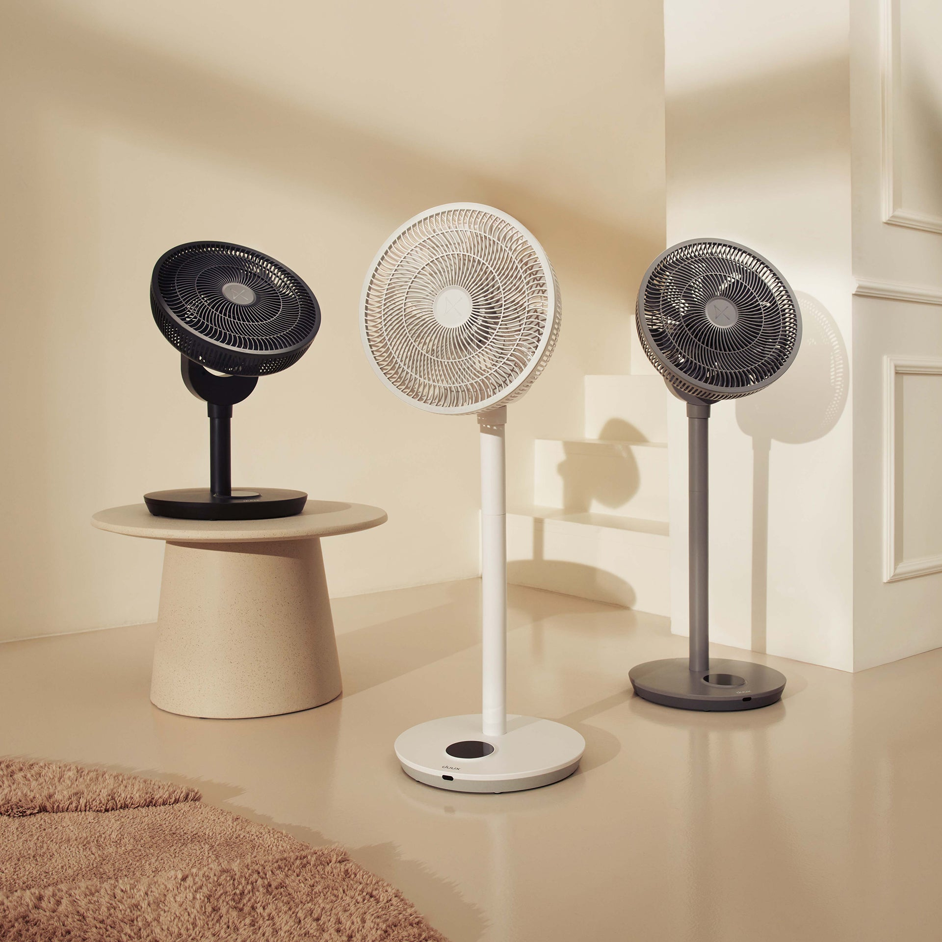 Trois ventilateurs noir, blanc et gris sur le sol.