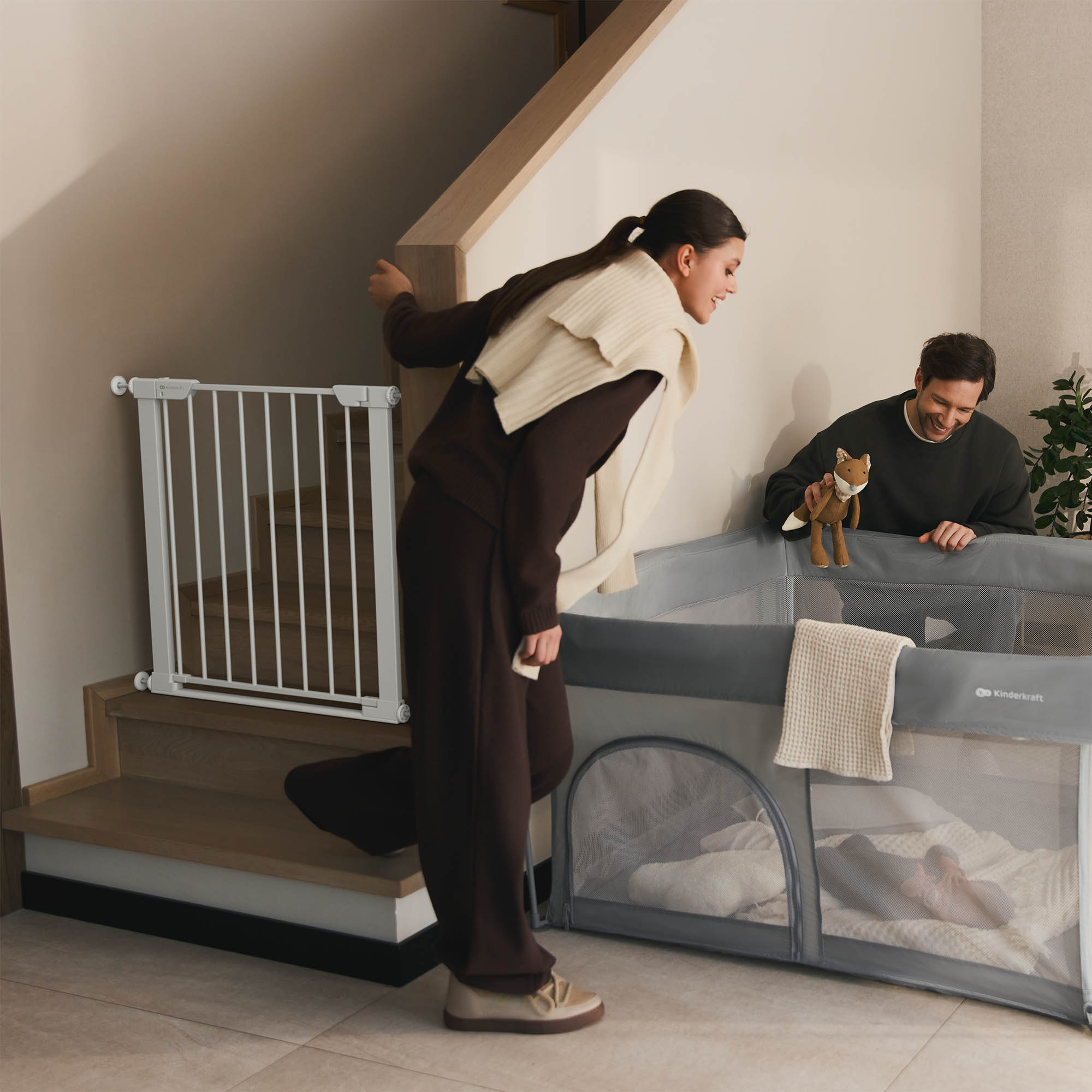 Mann und Frau nahe Laufstall. Frau an Treppe mit Gitter. Fuchspielzeug auf Laufstall.