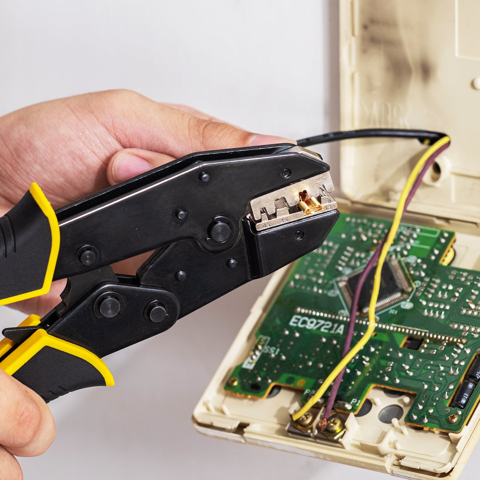 Eine Hand benutzt eine Crimpzange, um ein Kabel an einer Leiterplatte anzuschließen.