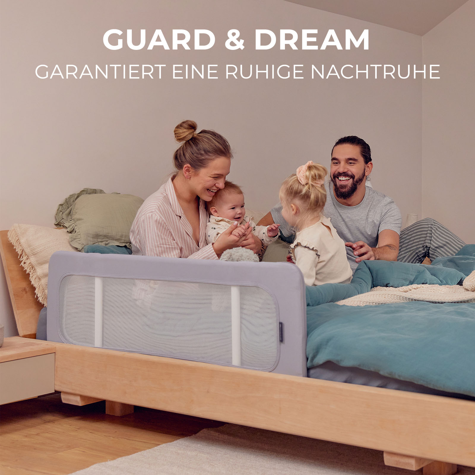 Familie im Bett mit Baby-Bettgitter. Mutter, Vater und zwei Kinder.