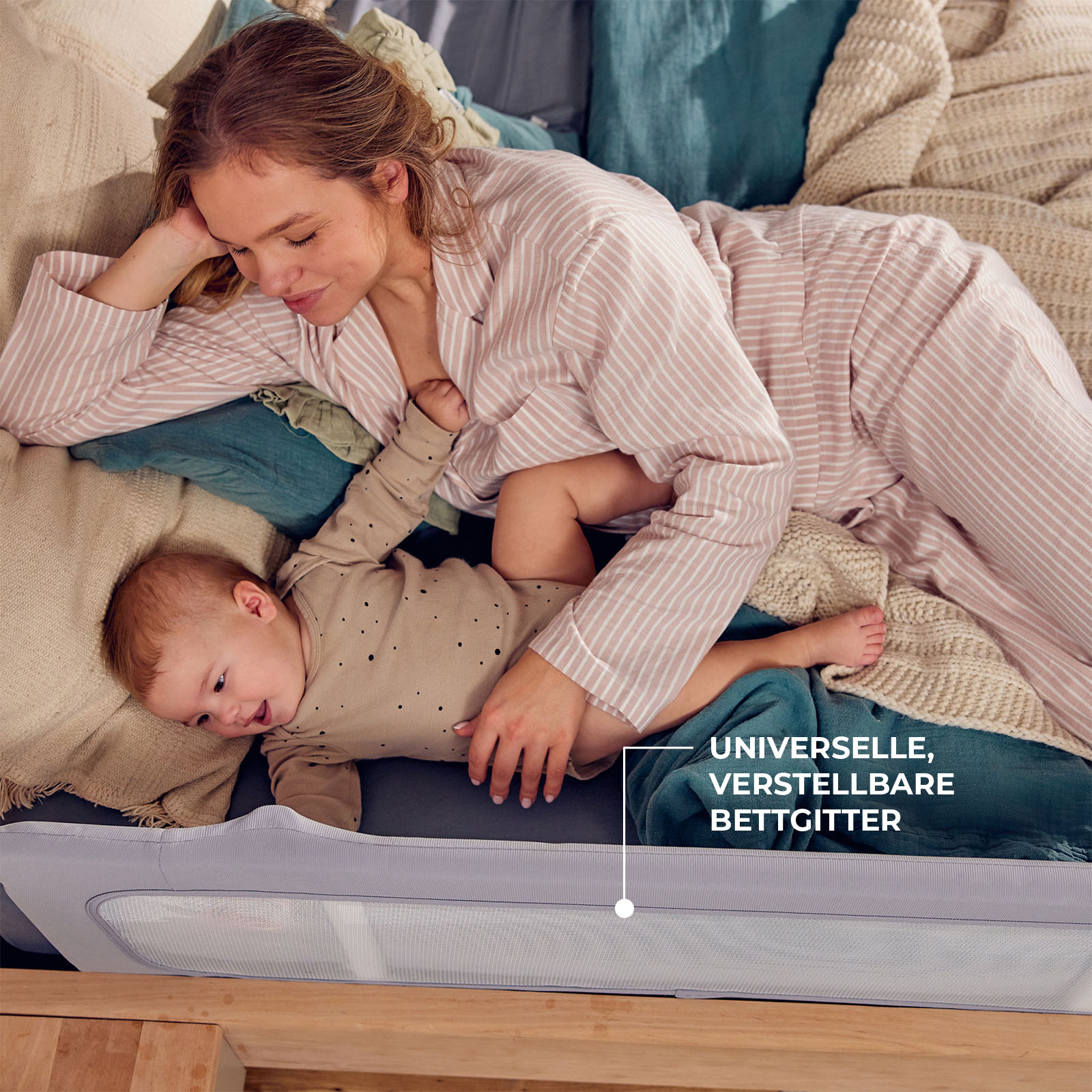 Eine Frau in gestreifter Kleidung liegt mit einem Baby auf einem Bett, das von einem Bettgitter gesichert ist.