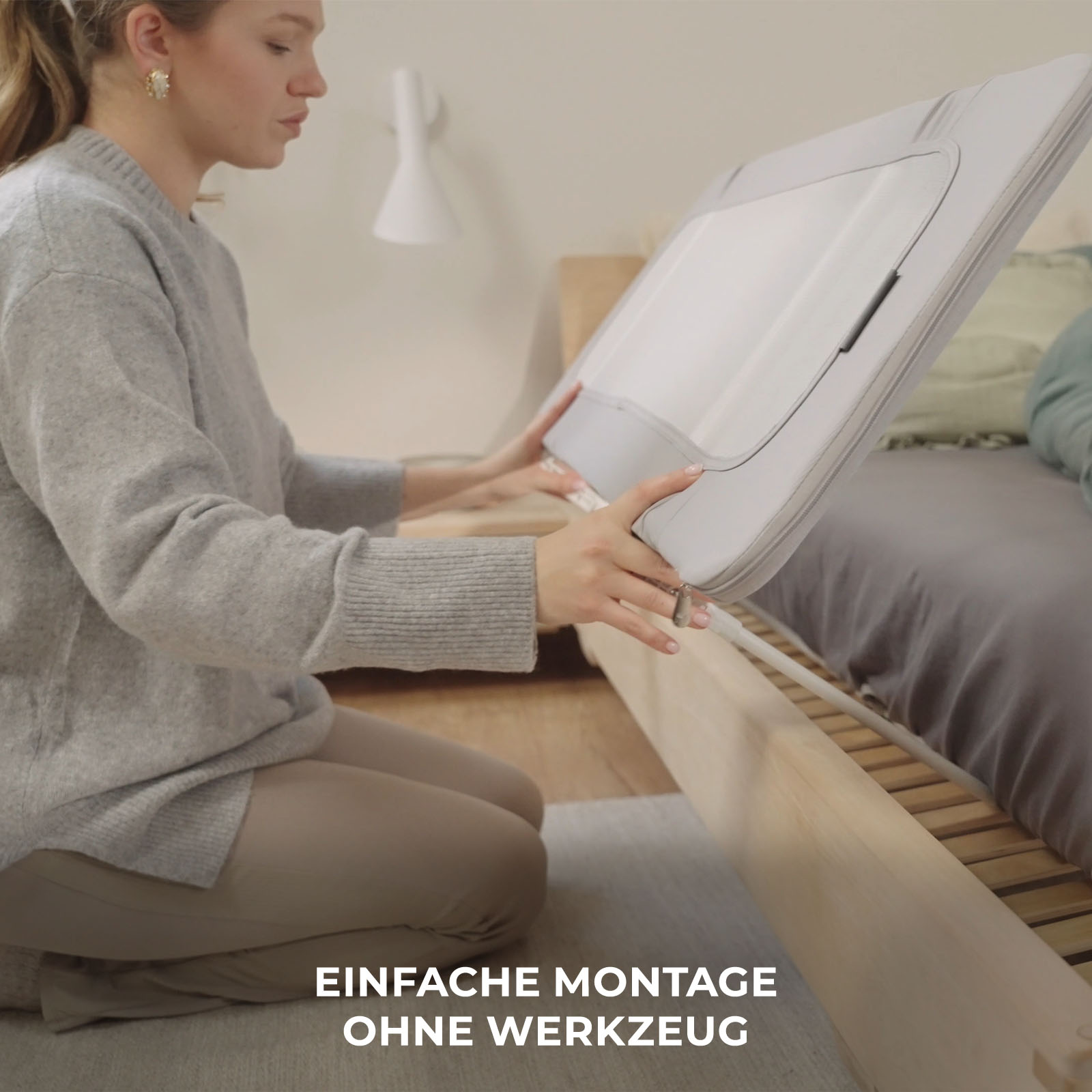 Frau sitzt auf dem Boden und hält ein graues Babybett-Zubehörteil.