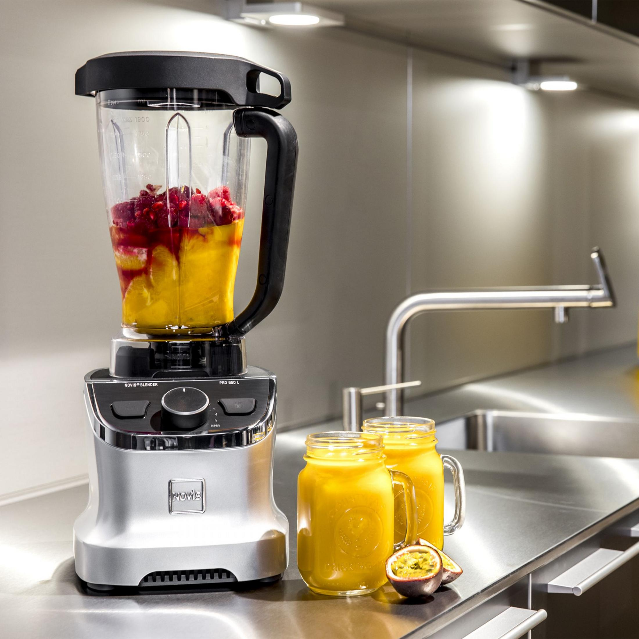 Un frullatore con frutta e due bicchieri di succo su un piano di lavoro.