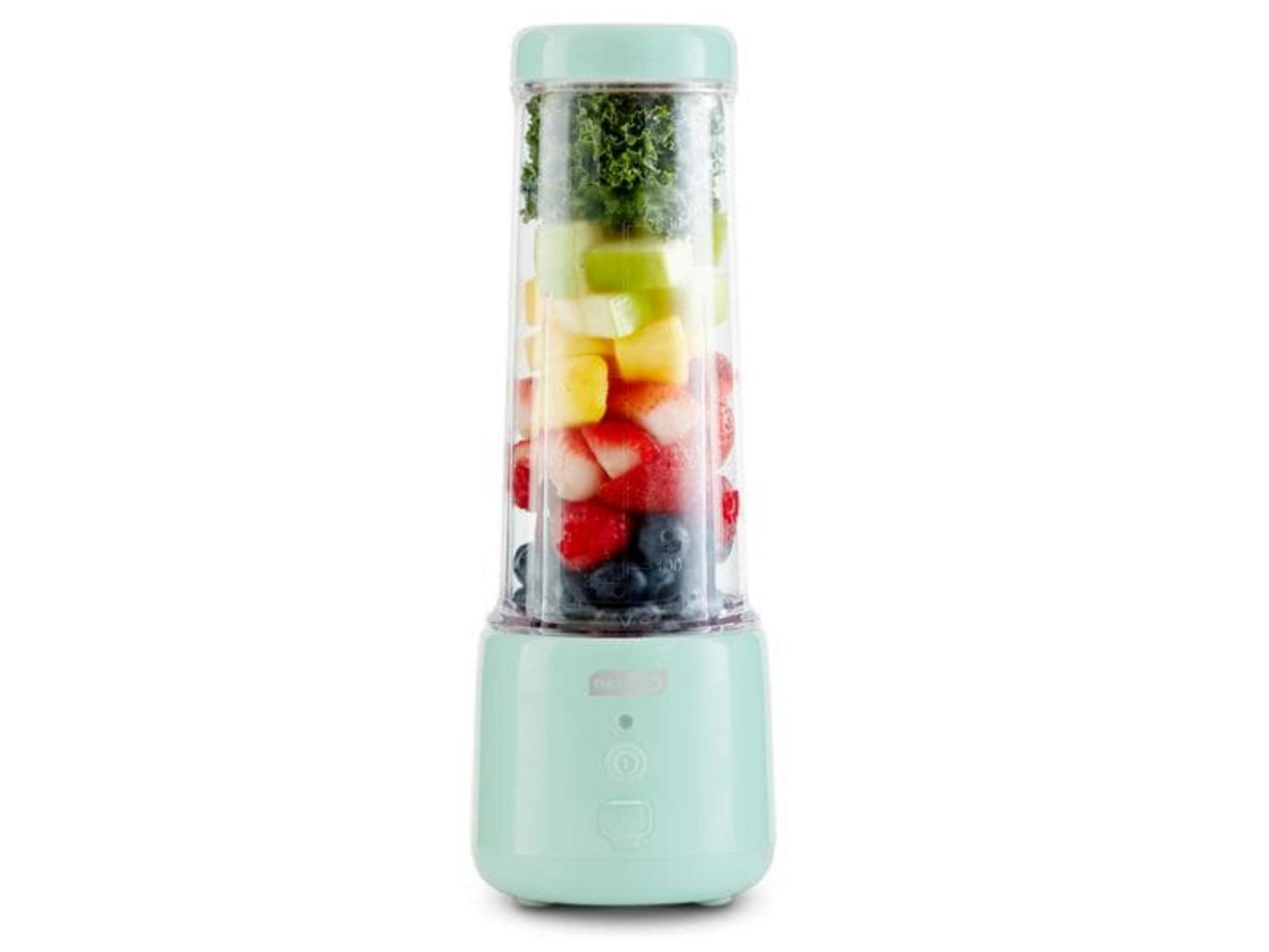 Ein mintgrüner Mixer gefüllt mit geschichteten Früchten: Blaubeeren, Erdbeeren, Ananas, Apfel, Grünkohl.