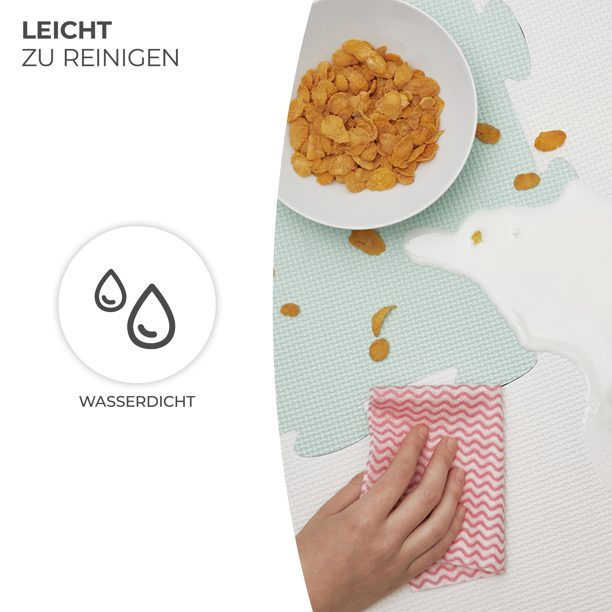 Eine Hand wischt verschüttete Milch mit einem rot-weißen Tuch von einer Spielmatte.