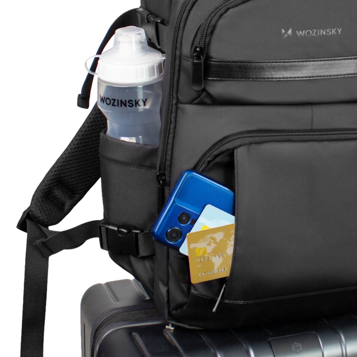 Zaino nero con borraccia, telefono e carte nelle tasche. Valigia sotto.