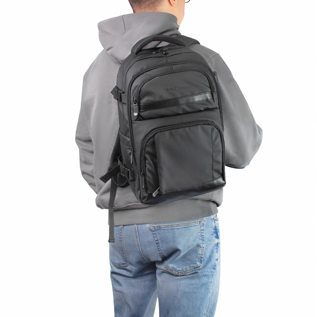 Una persona con felpa grigia e jeans blu indossa uno zaino nero.