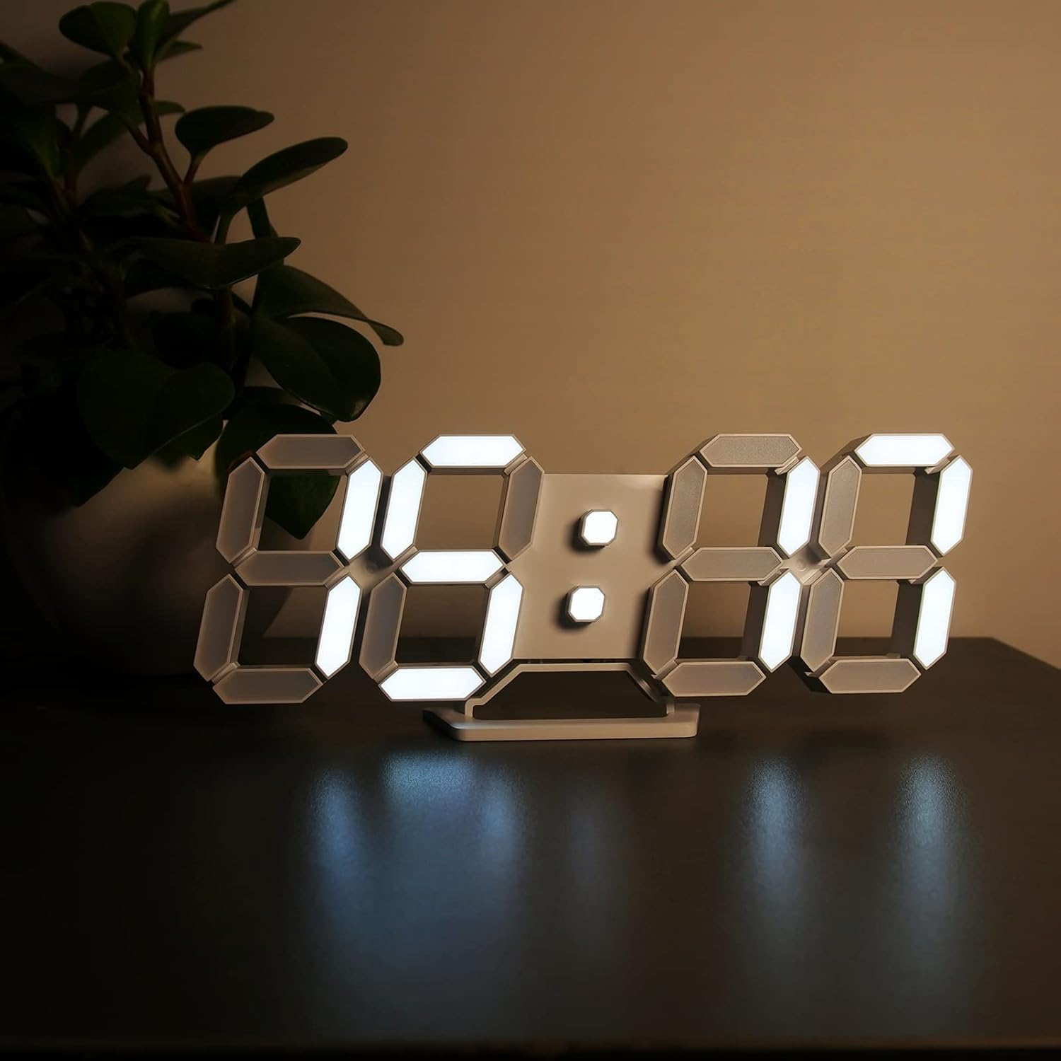 Ein digitaler Wecker mit weißen Ziffern auf einem dunklen Tisch, daneben eine Pflanze.