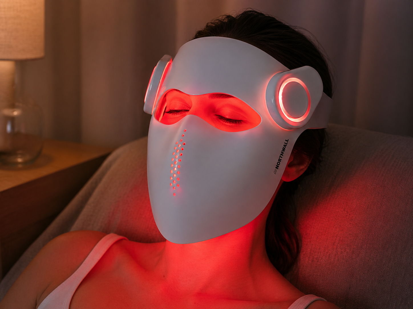 Een vrouw met gesloten ogen draagt een wit LED-gezichtsmasker met rood licht.