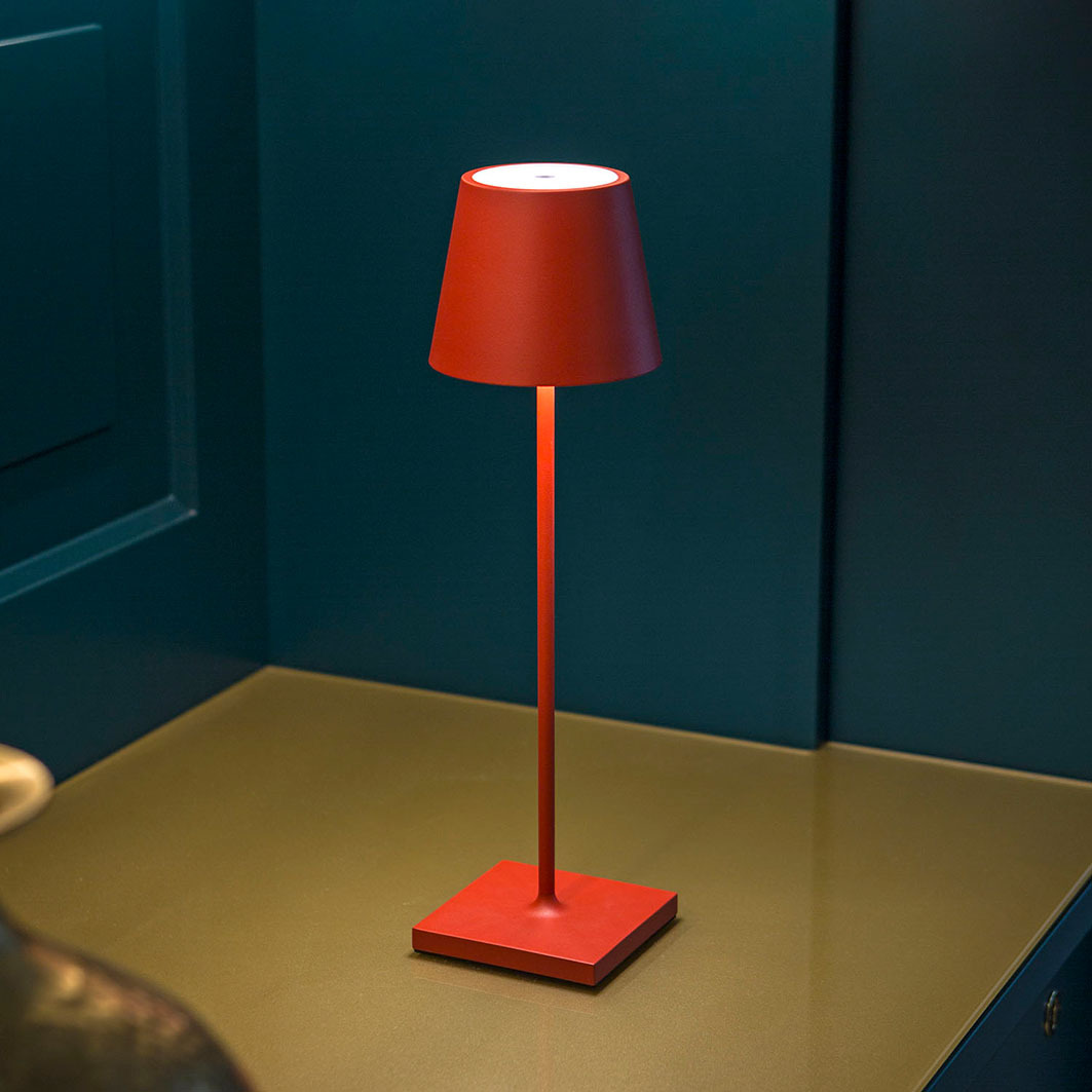 Eine rote Tischlampe mit schmalem Ständer steht auf einem Tisch.