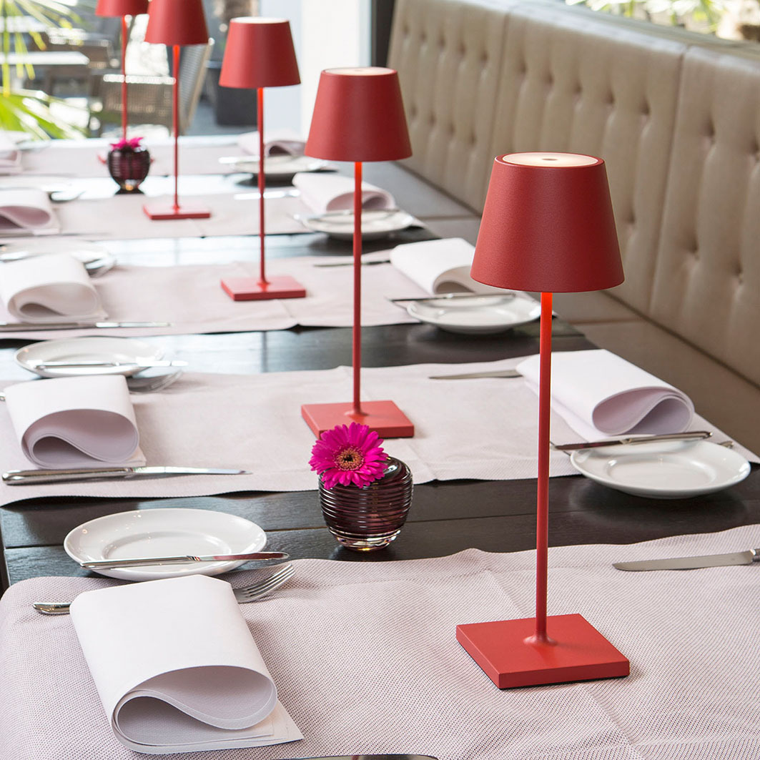 Rote Tischlampen und Blumen auf einem gedeckten Tisch in einem Restaurant.