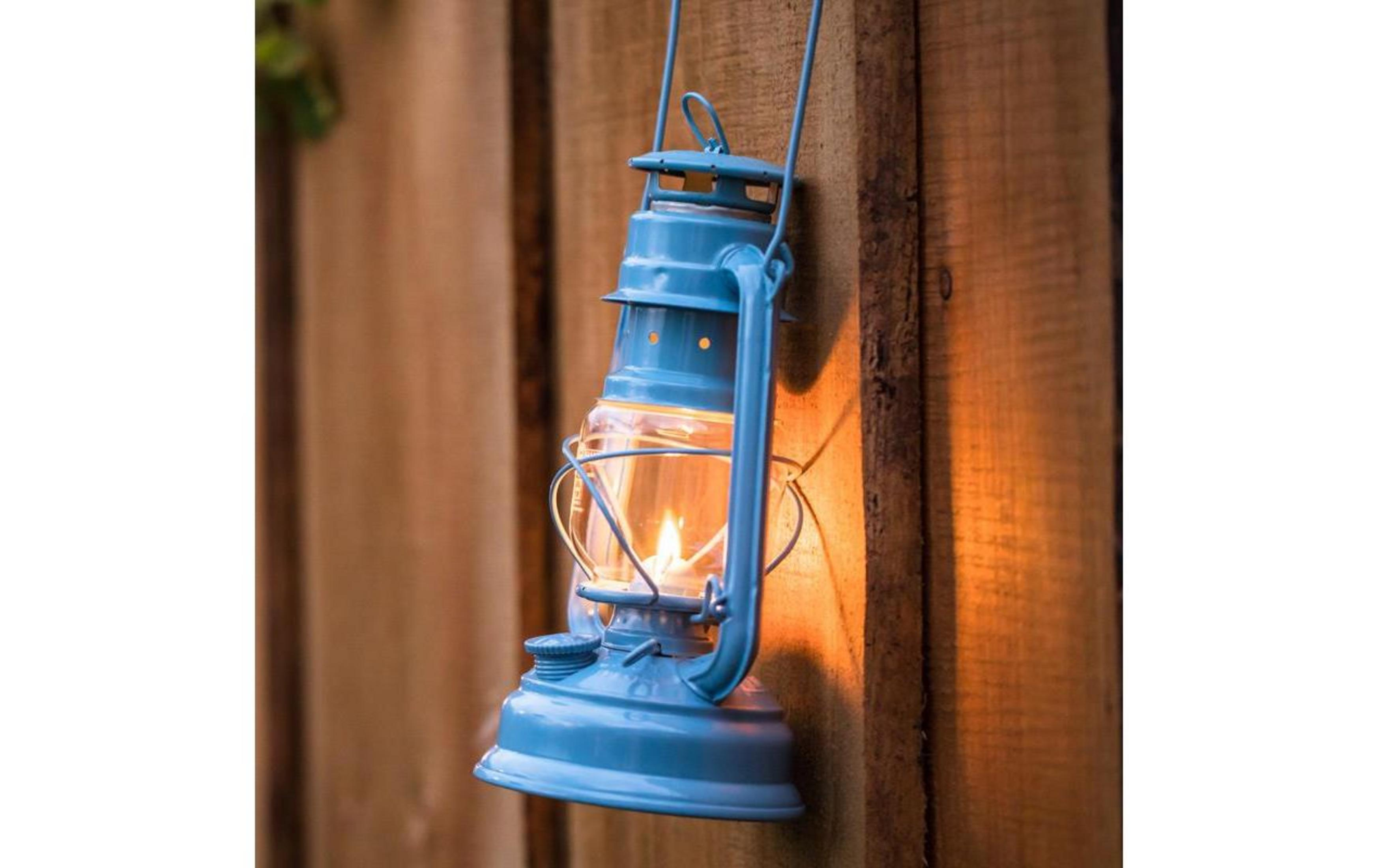 Eine blaue Laterne mit brennender Flamme hängt an einer Holzwand.