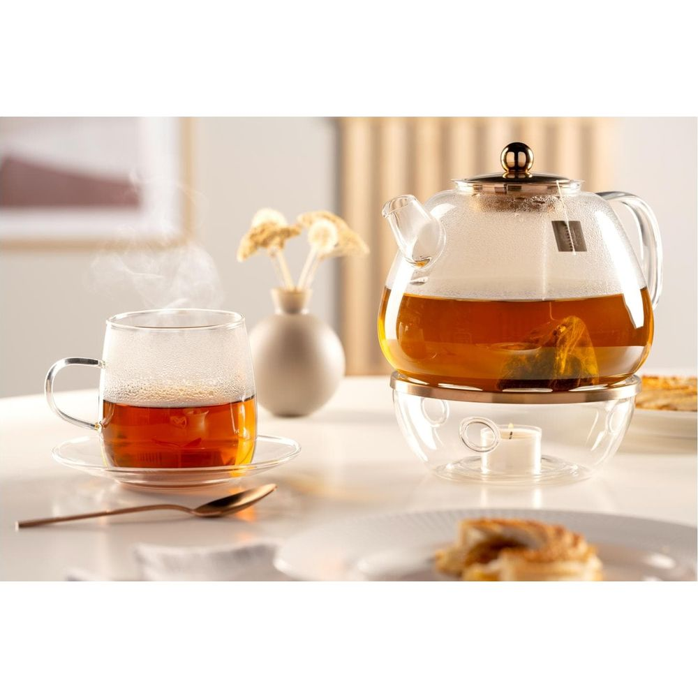 Glas-Teekanne mit Tee und Kerzenwärmer, daneben eine dampfende Teetasse.
