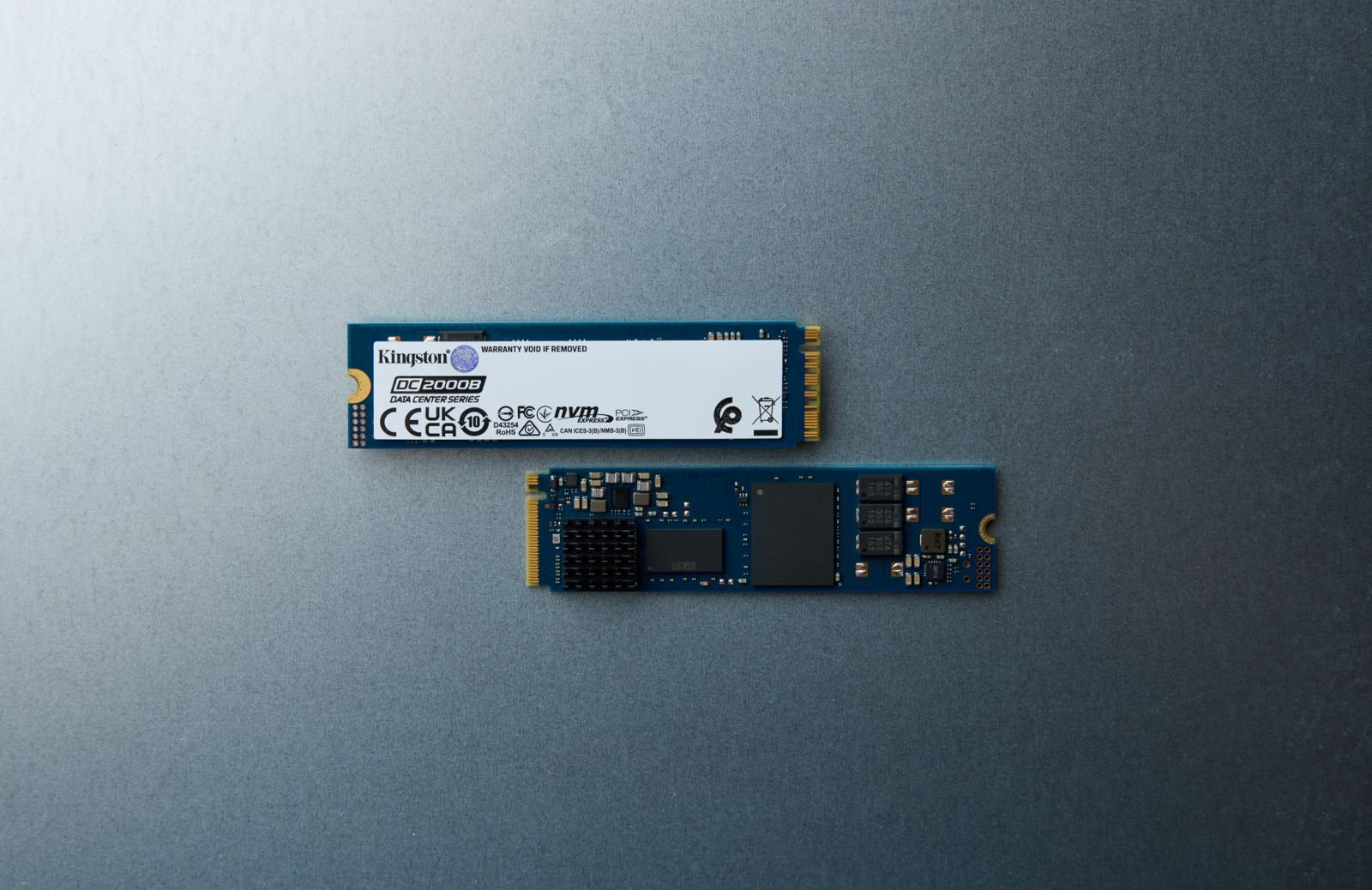 Two Kingston NVMe SSDs on a grey surface. One shows the label, the other shows the components.